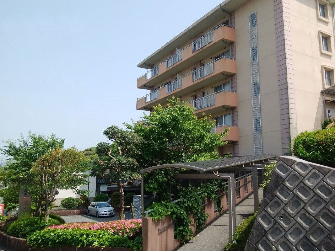 ６階建ての建物はブラウン系の外壁で、草木が植えられ、車が止まっている駐車場もある。