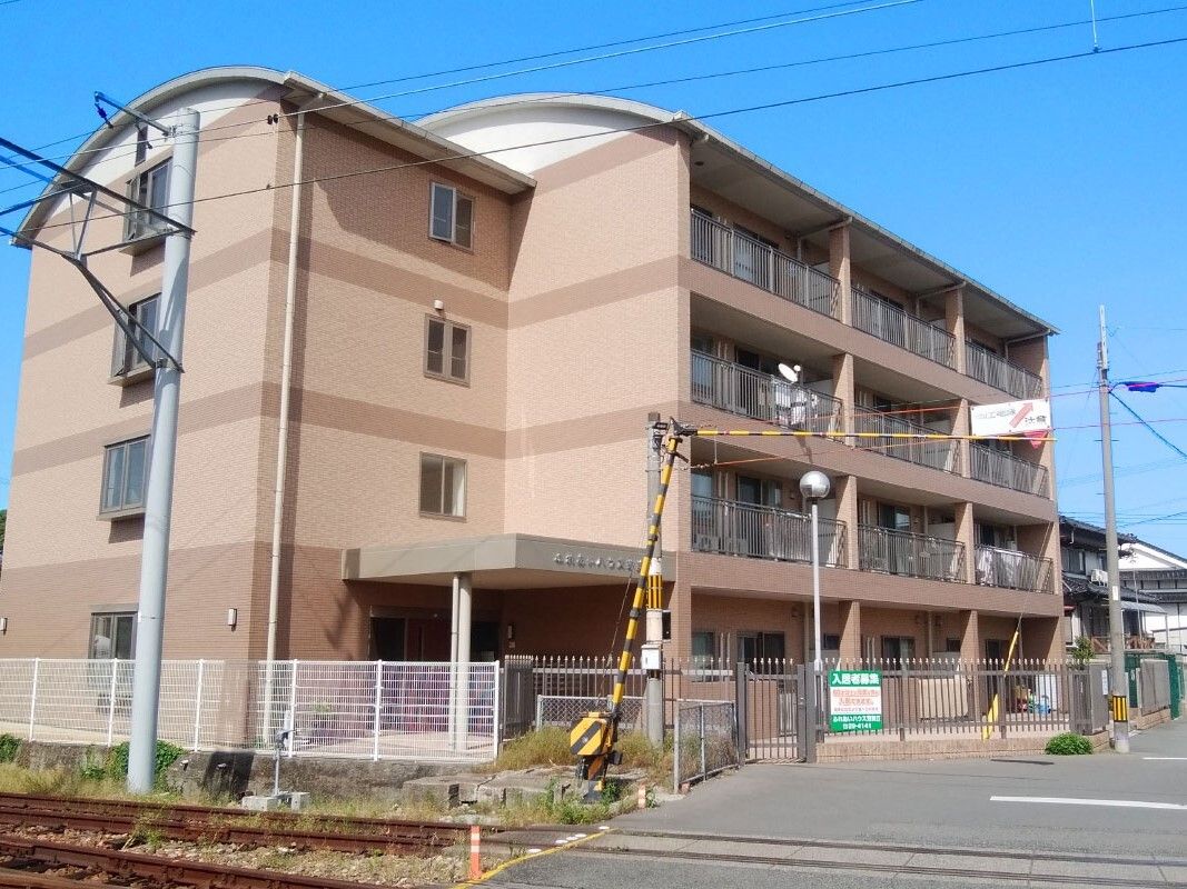 角フロアにベランダが付いた4階建ての建物の前には踏切がある。日当たりのいい場所に建っている。