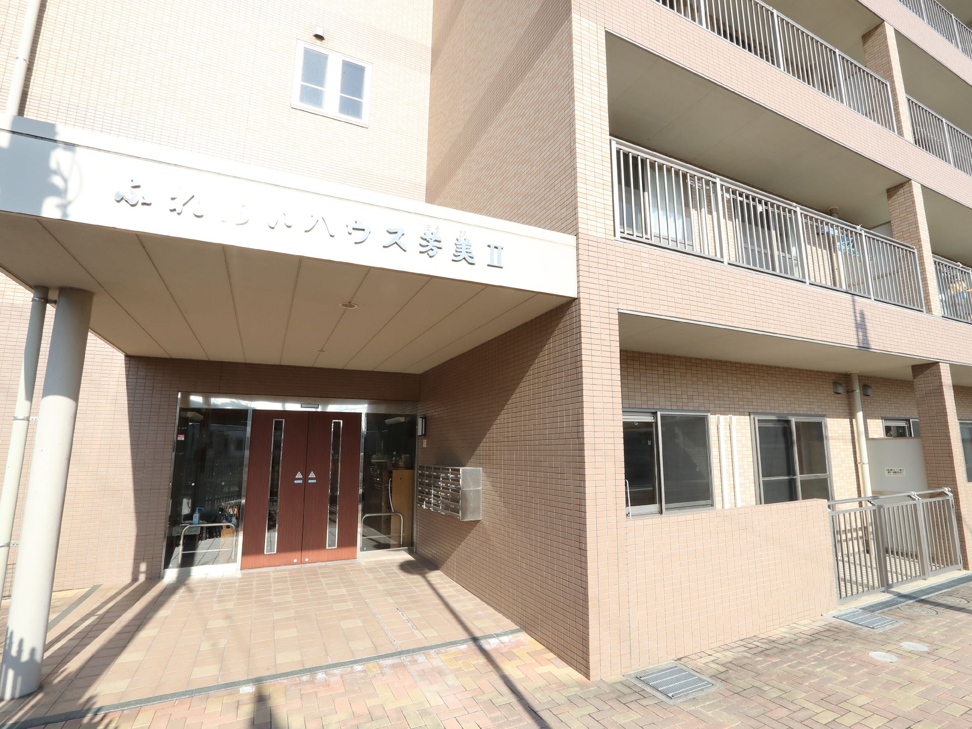 ブラウン系の4階建ての建物の前には踏切があり、日当たりのいい場所に建っている。
