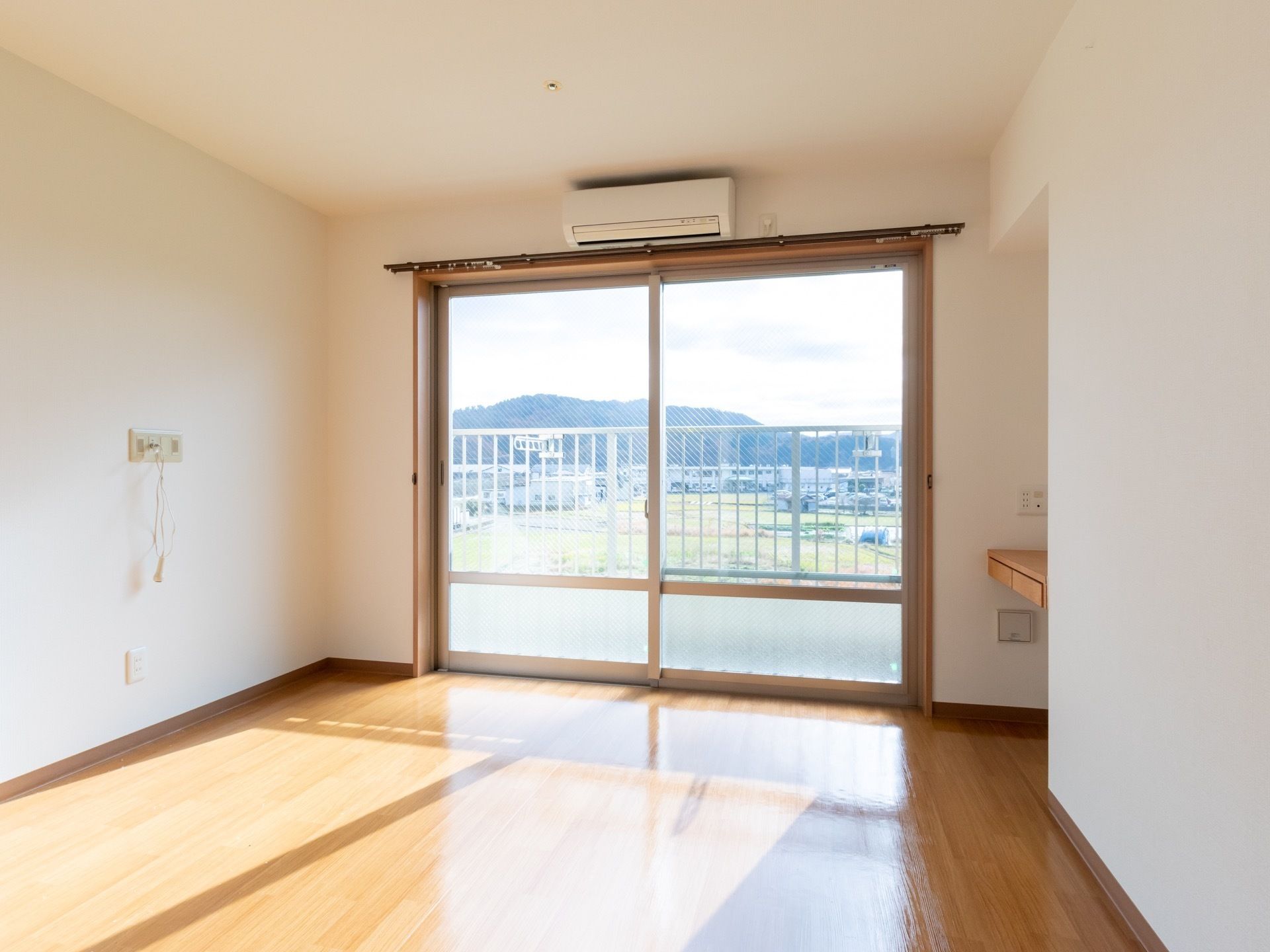 大きな窓のある居室である。窓の外にはベランダが設置されており、窓の上にはエアコンが取り付けられている。