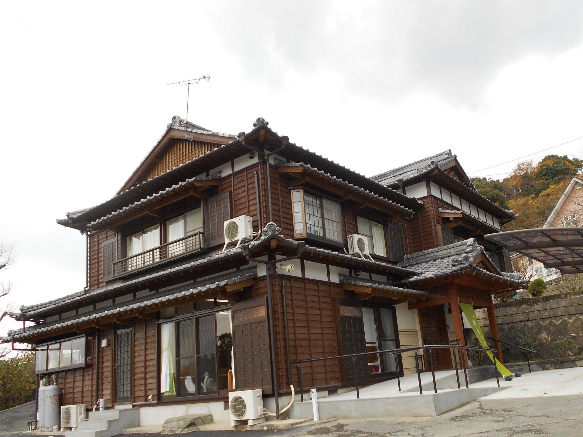 瓦屋根が印象的な２階建ての住宅がある。敷地の隅に白い軽トラックが停まっていて、横に空の植木鉢やプランターが積まれている。