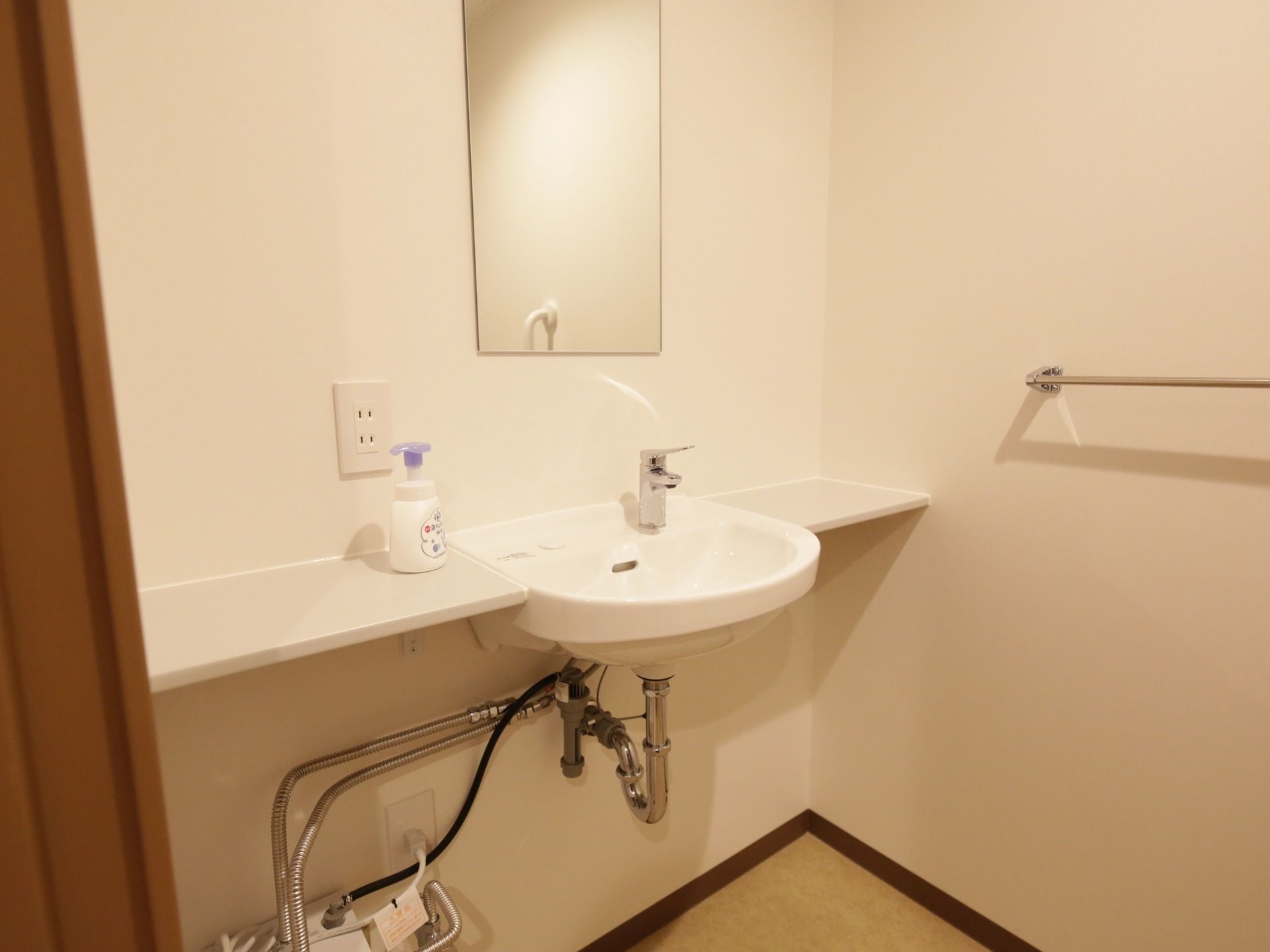 居室の広いトイレに設置されている洗面台。台が付いており、正面に大きな鏡が付いている。壁にはタオルハンガーがある。