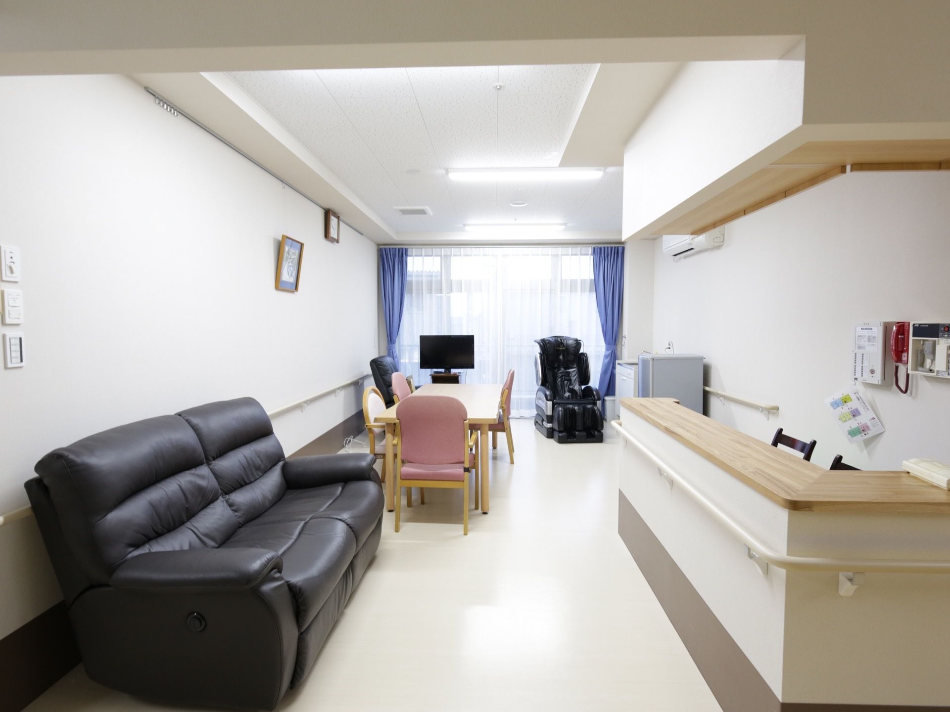 縦長の細長い部屋がある。壁は白く、突き当りには大きな窓がある。テーブルと椅子、テレビ、黒いソファが置かれており、手前にはカウンターがある。