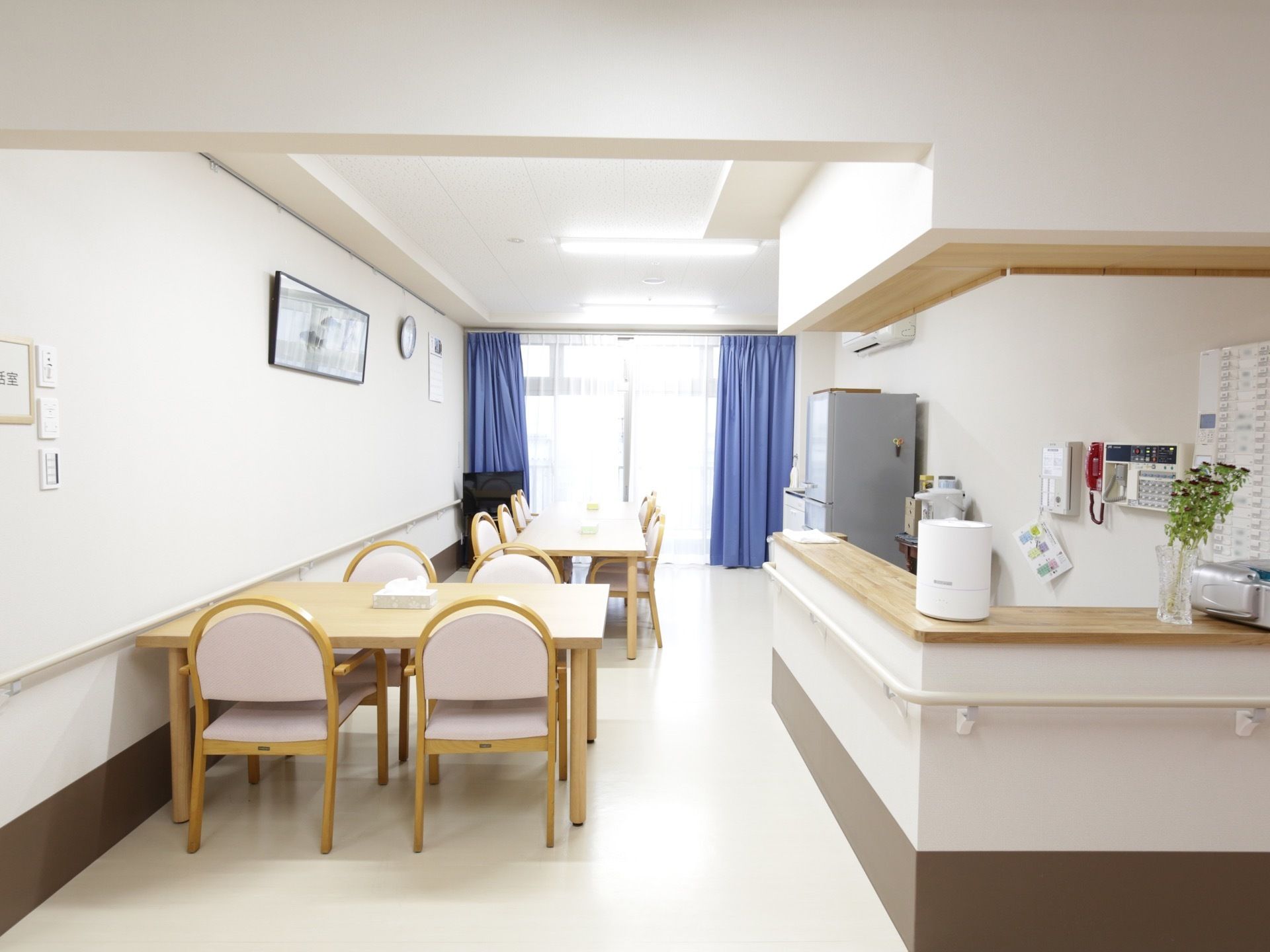 突き当りに窓のある、縦長の部屋である。大きなテーブルが２つあり、ピンクの背もたれの椅子がたくさん置かれている。手前にはカウンターがある。
