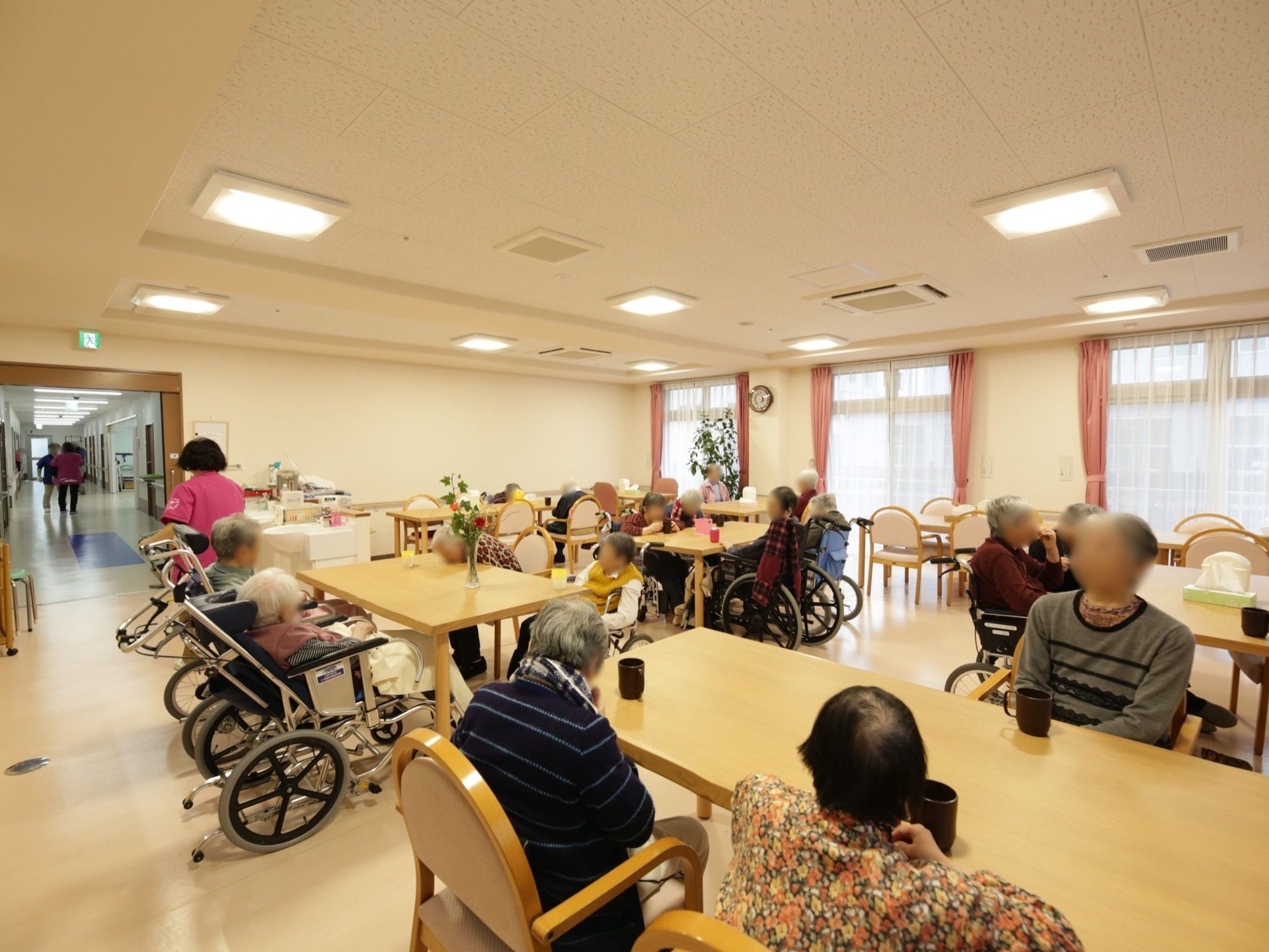 広い空間に、テーブルと椅子がたくさん置かれている。大きな窓が並んでおり、大勢の入居者様が席に座られている。