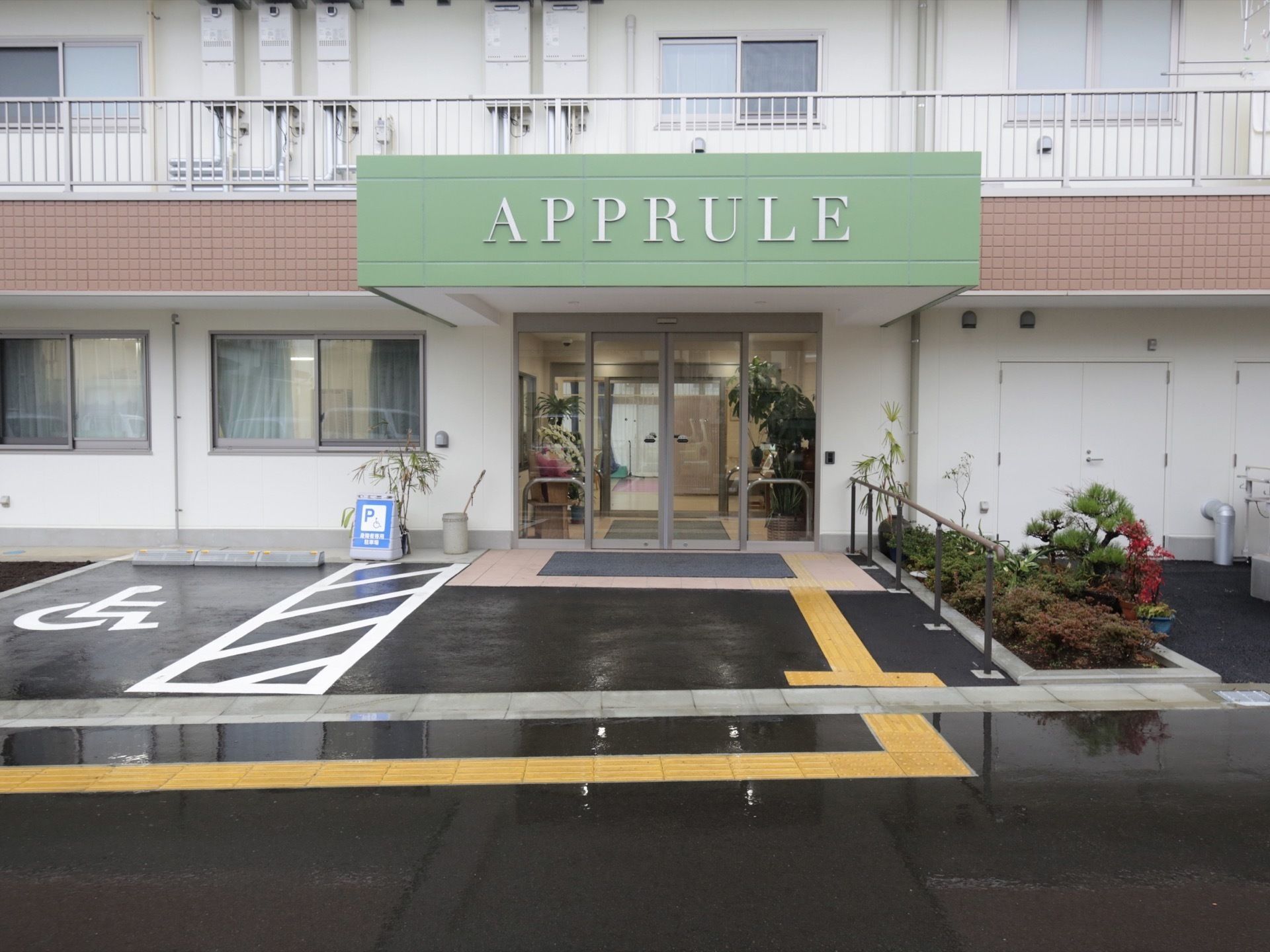 鉄骨造3階建ての建物の外観。手前に駐車場スペースがある。