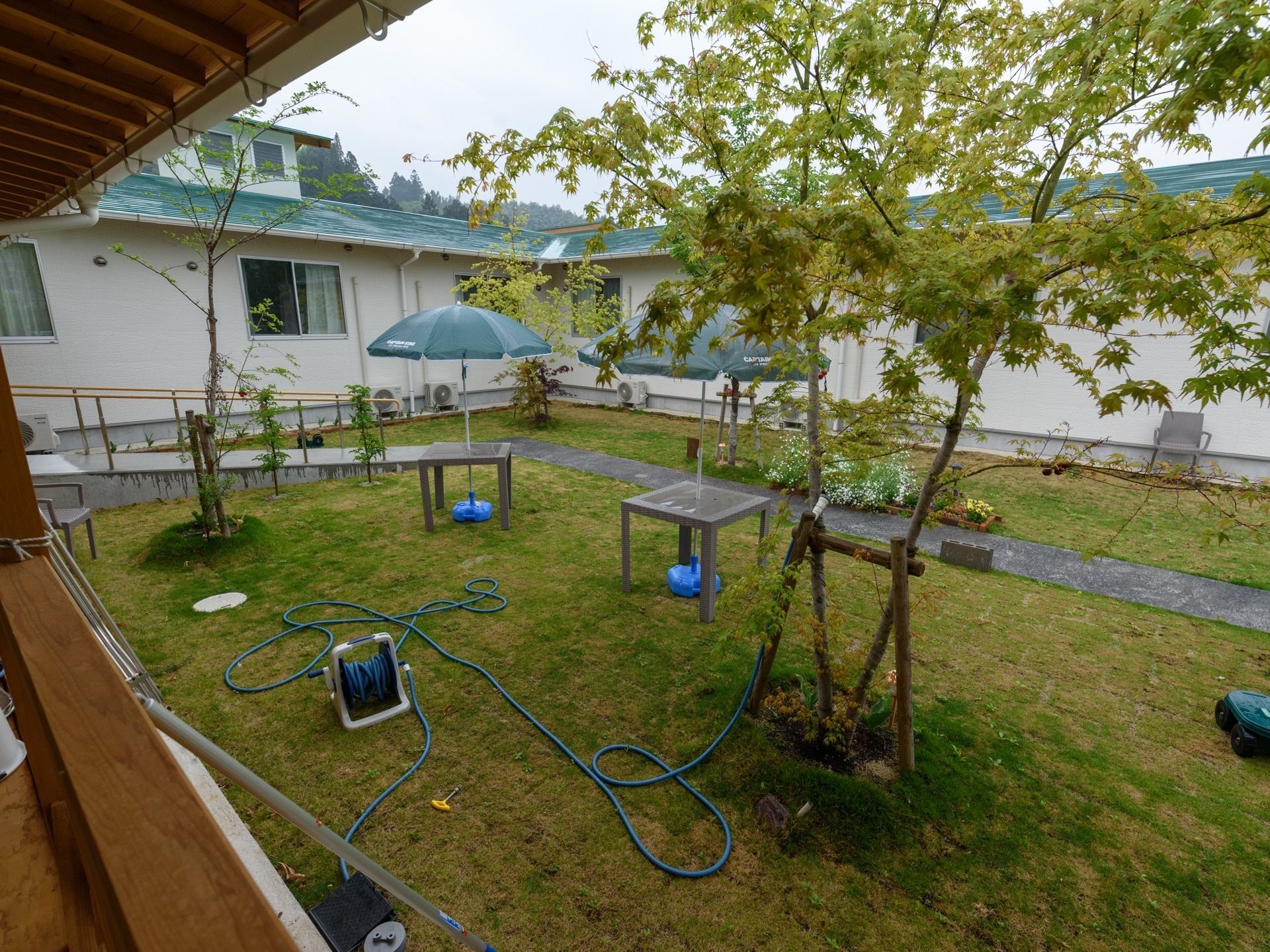 建物から伸びているスロープの先には、舗装された道が続いている。芝生が茂っている庭に、パラソルやホースが置いてある。