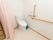 トイレの右横の壁には、オレンジ色の緊急呼出ボタンが設置されている。青色の小さいゴミ箱が、便器のすぐ側に置いてある。