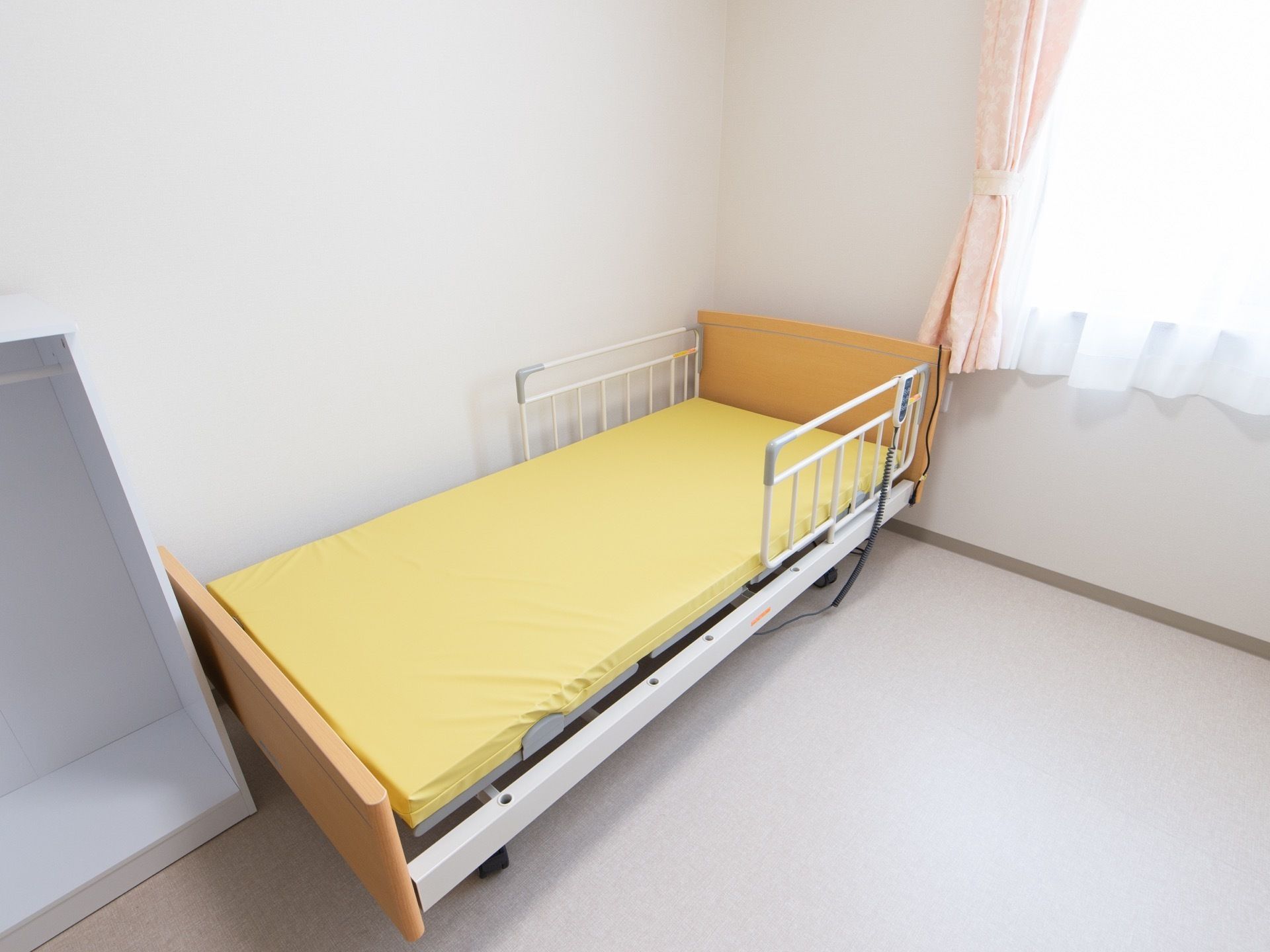 各居室備えつけの介護ベッド。左右に転落防止フェンスがある。布団を敷いていない状態のマット部分は黄色になっている。