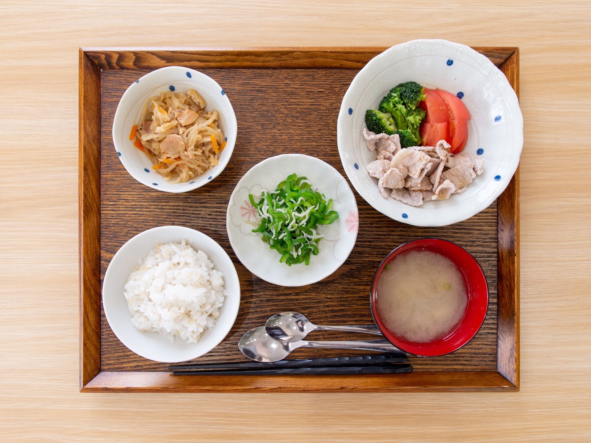 お盆に、せん切り大根の煮物、しらすの入った野菜の和え物、お肉の野菜添えなどの皿とごはん、みそ汁が並んでいる。