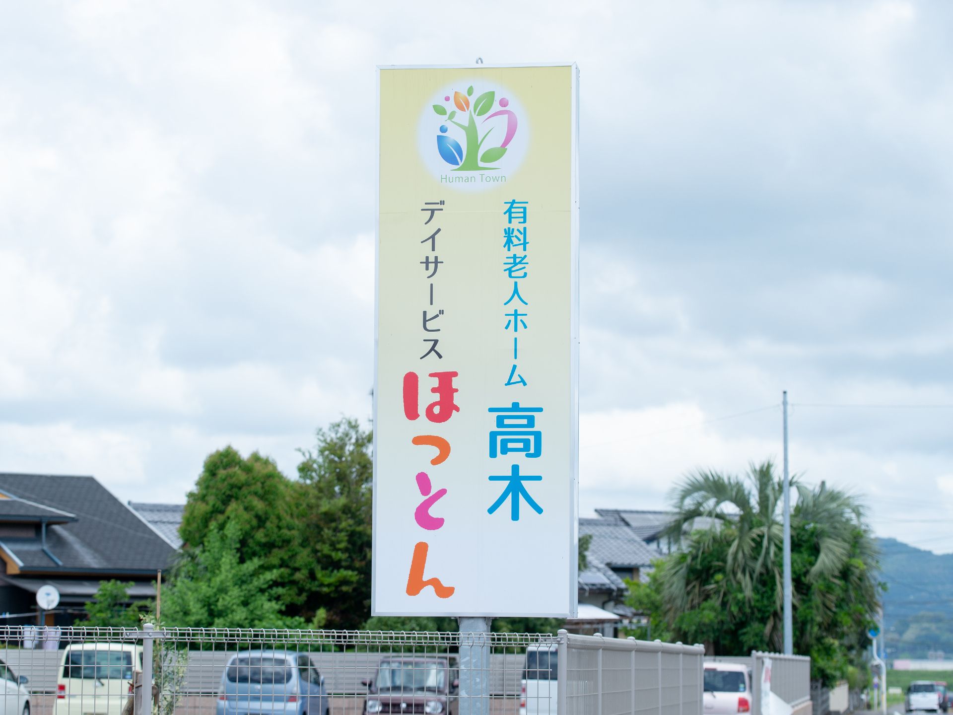 駐車場のフェンス際に立てられた施設名称と種別がロゴマークと共に明記された看板