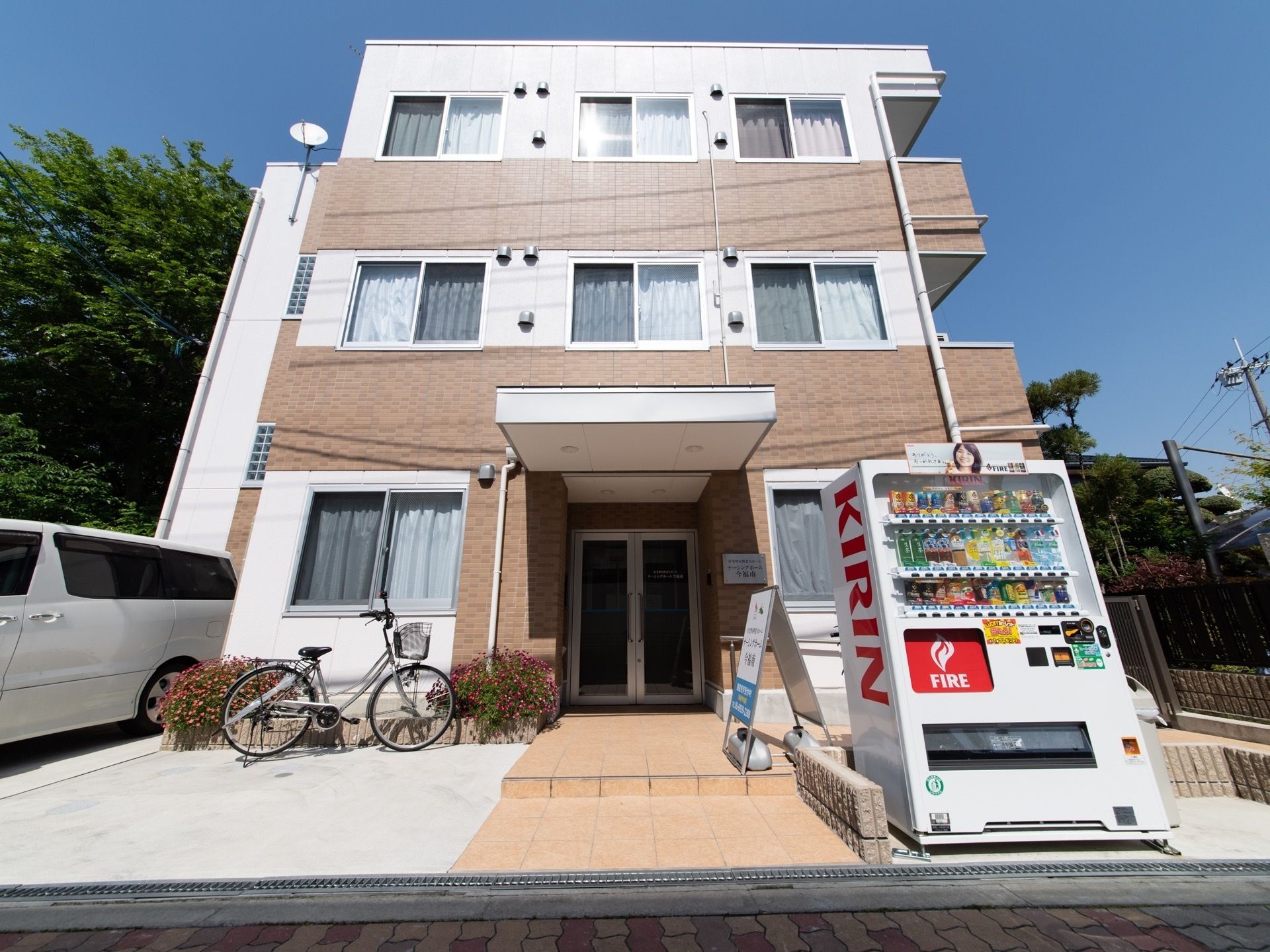 白とレンガ調を基調とした外観の３階建ての建物である。玄関ドアの前方に１段の階段があり、自動販売機を設置している。