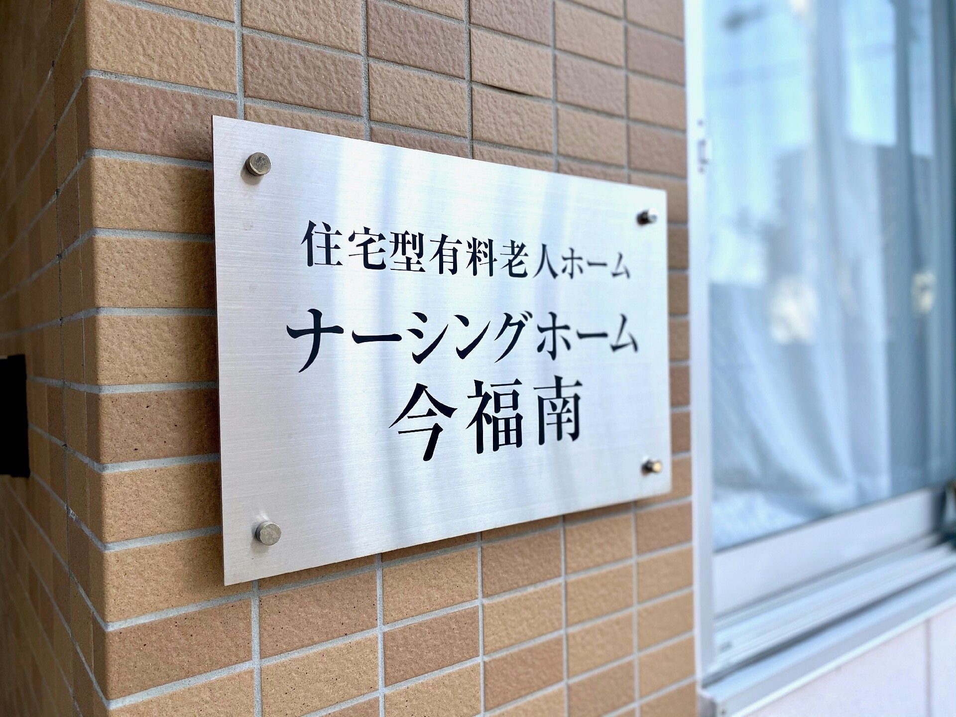 ピンクのエプロンをした女性スタッフがピンクのカーディガンを着た高齢女性のそばに寄り添い、二人は楽しそうに笑っている。