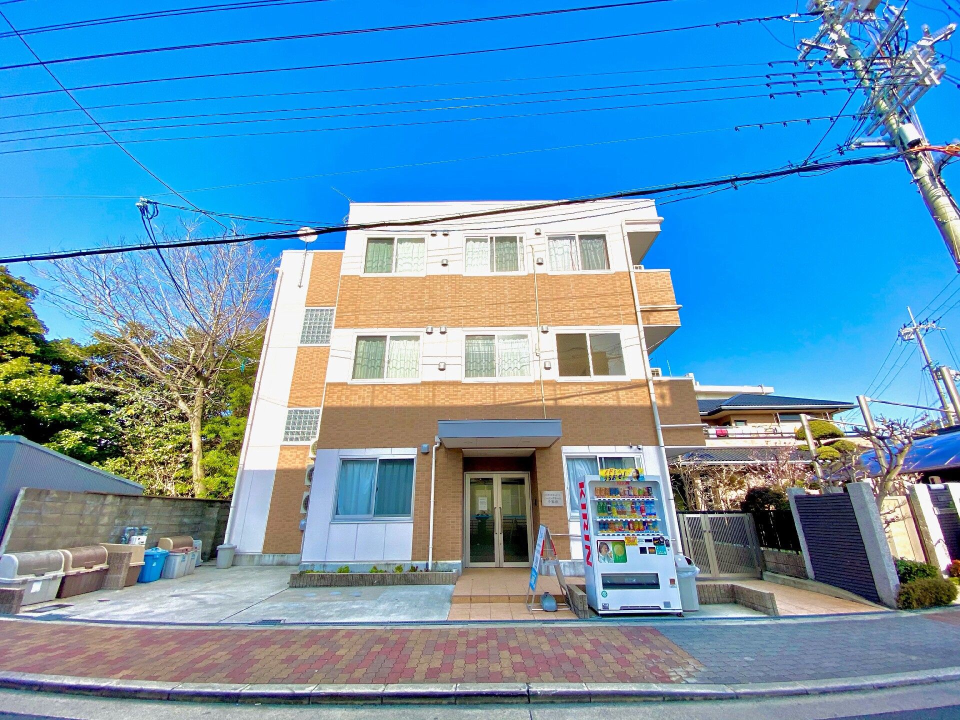 屋外で車いすに座った高齢女性が誰かに向かって笑顔で手を振っている。若い男性スタッフに車いすを押してもらっている。