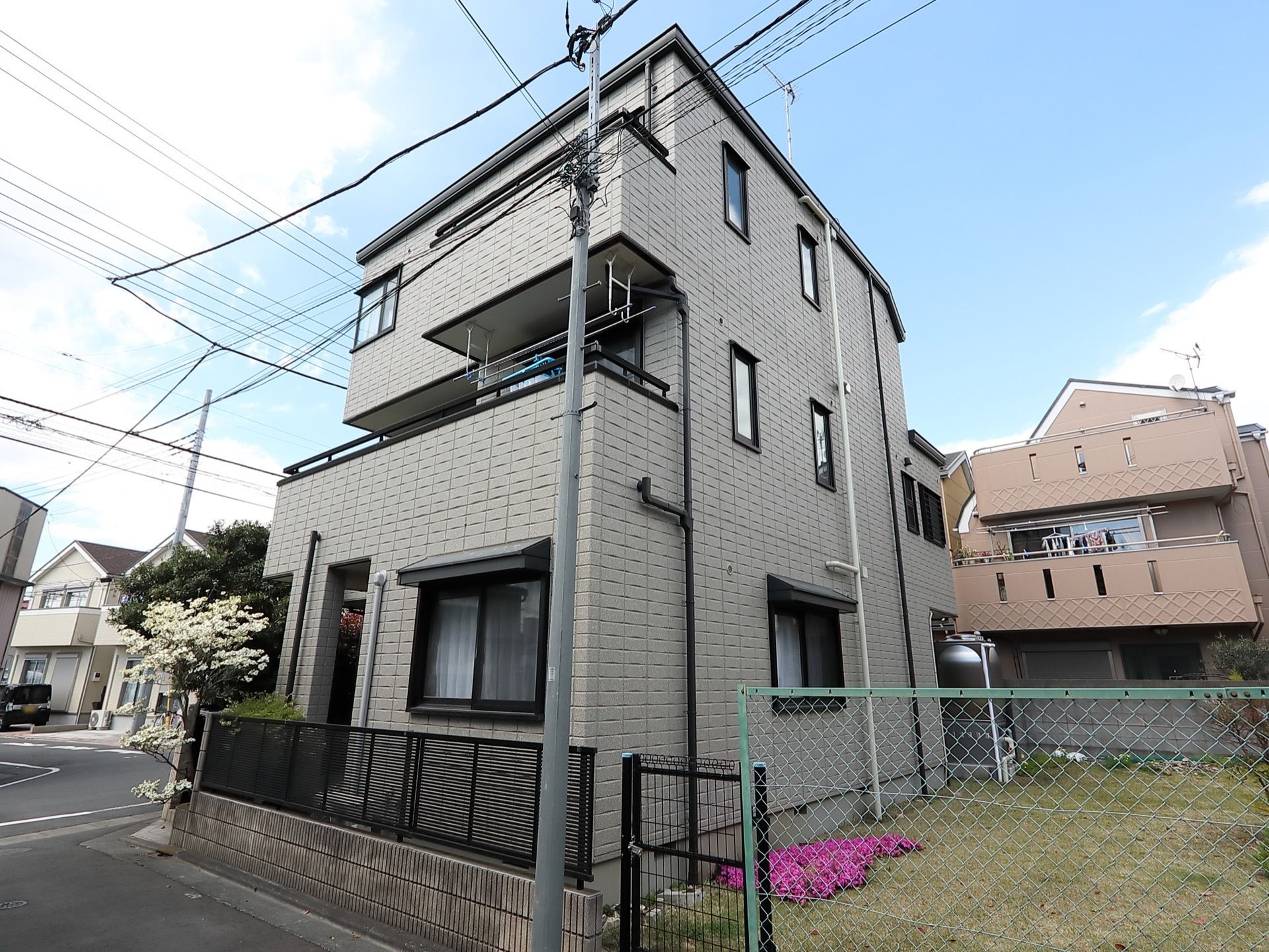 ３階建ての一軒家のような外観の施設である。２階のバルコニーに洗濯物が干されている。隣は空き地である。