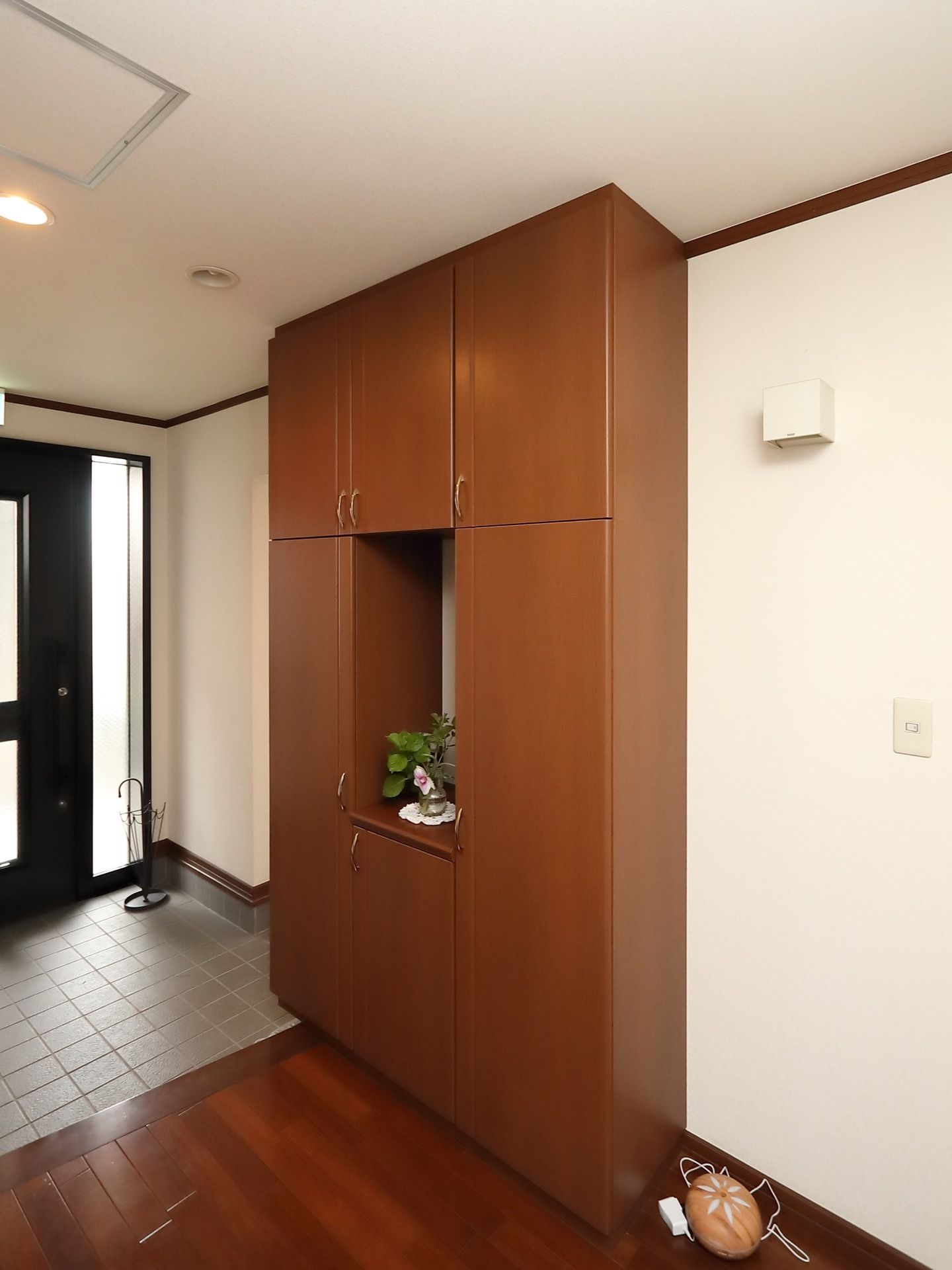 玄関の土間に傘立てが置かれている。土間を上がった所に、天井までの高さがある、扉が６枚ついた収納棚が設置されている。