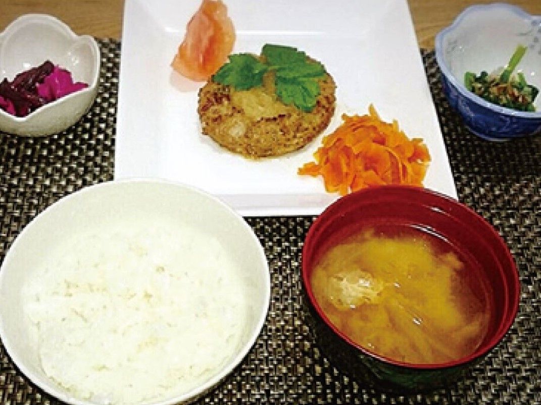 白いご飯にみそ汁、小鉢などが並んだランチョンマット。肉料理がメイン。