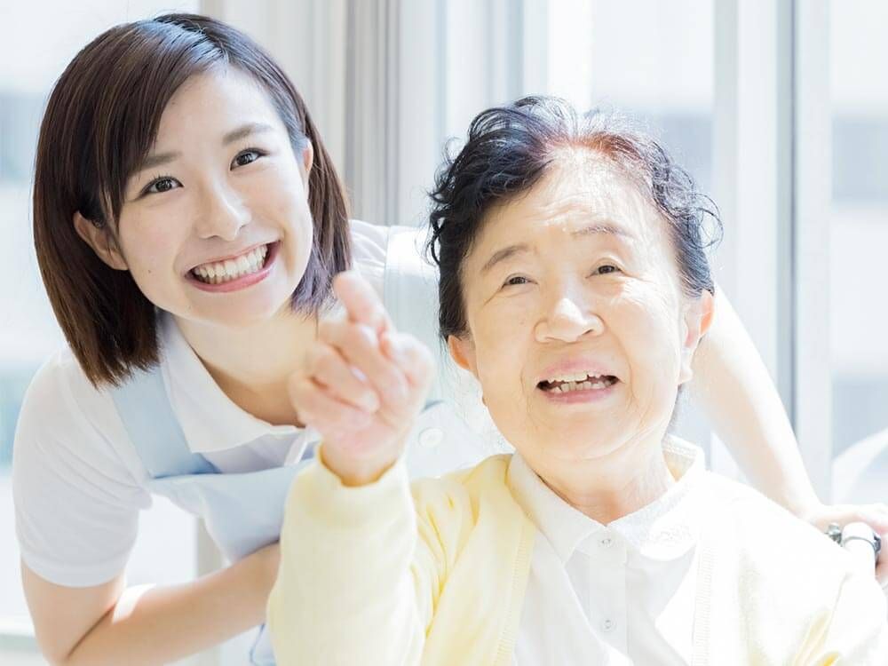 前を指差す高齢女性と笑顔で見上げる女性ヘルパー