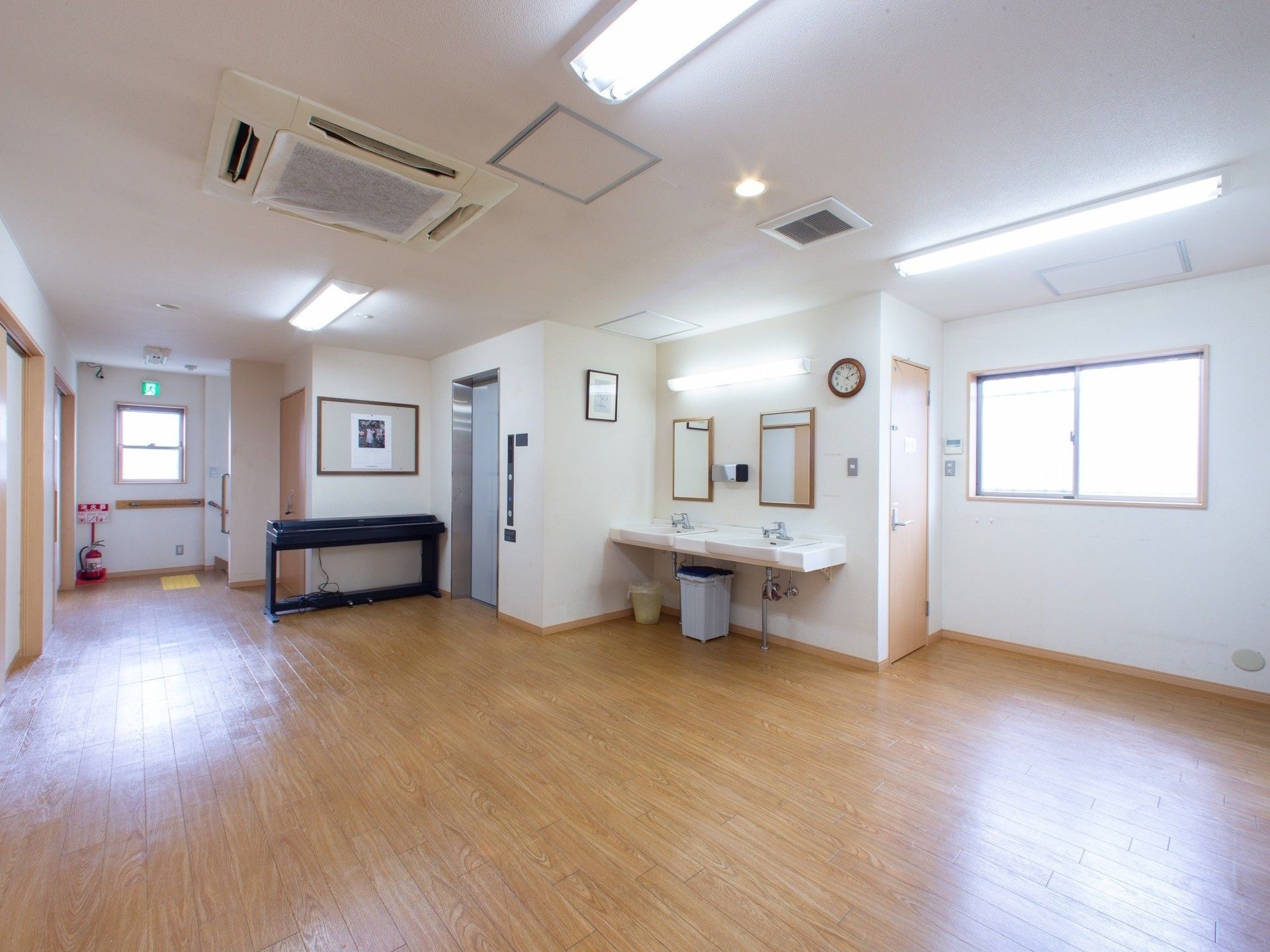 明るい白色の外壁の建物である。壁には水色の横長な看板が設置され、看板の左右にはライトが取り付けられている。