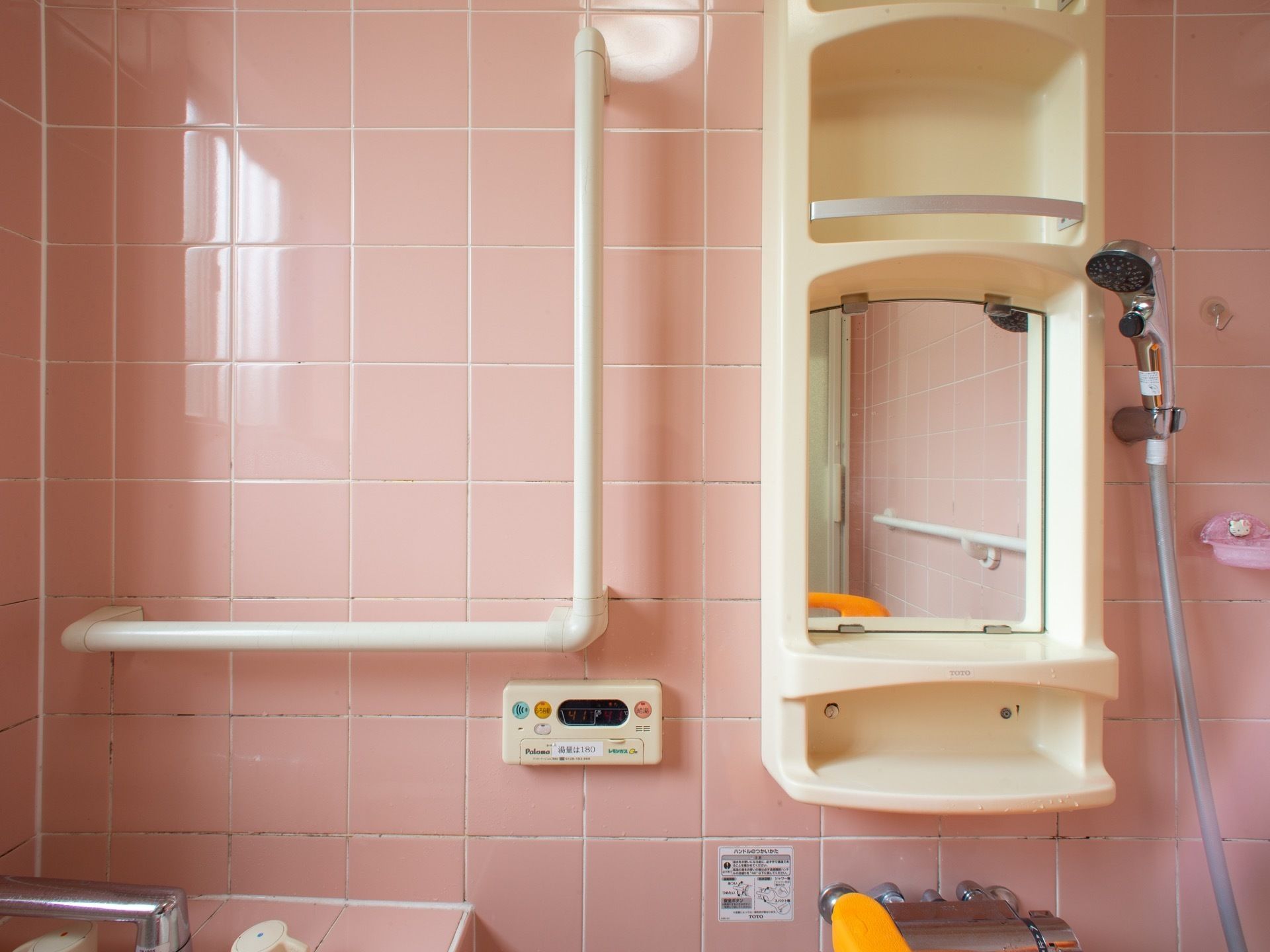 浴室内の洗い場には、鏡付きの棚が設置されている。棚の横にはL字型の手すりと、給湯器の操作パネルが設置されている。