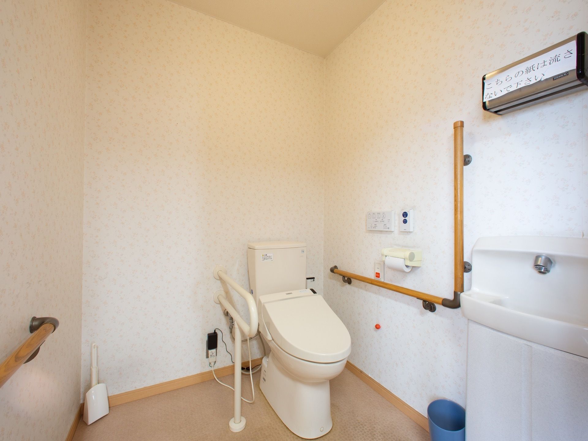 便器の両脇と入り口側の壁には、手すりが設置されている。手洗い器は、入り口側に独立して設けられている。