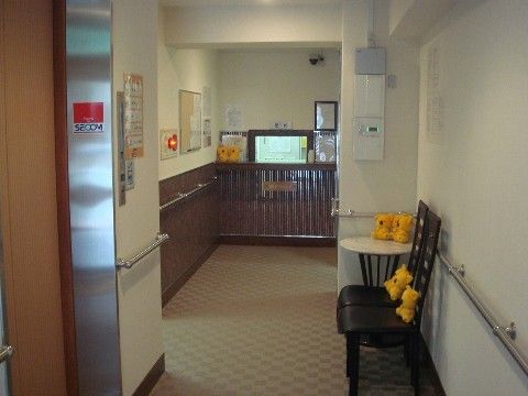 ベージュの床に白い壁の廊下。通路に置かれた椅子にはコアラのぬいぐるみが置かれている
