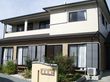 一般の住宅のような2階建ての建物が建っている。敷地内には植物が植えられ、門には住宅名が書かれている。