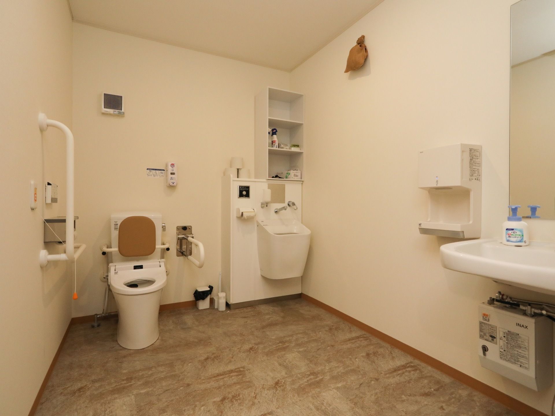 車椅子でご利用いただける広いトイレがある。壁には手すりとひじ掛けが設置され、便座に背もたれが付いている。室内には洗面台がある。