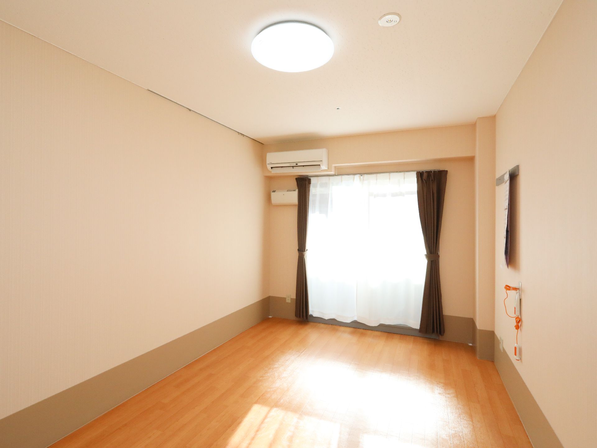 高さのある窓やエアコン、緊急呼び出しブザーが設置されたご入居前の居室
