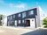 2階建ての建物は落ち着いた色合い。玄関前には屋根が付き、緑も多い。