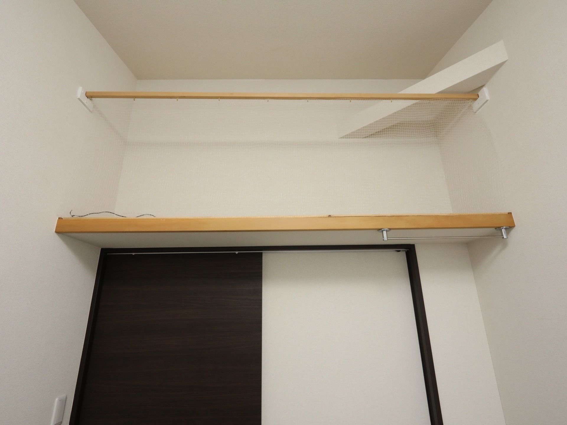 居室のドアの真上には、棚とネットを組み合わせた収納スペースがある。下の方にはハンガーなどを掛けるポールが付いている。