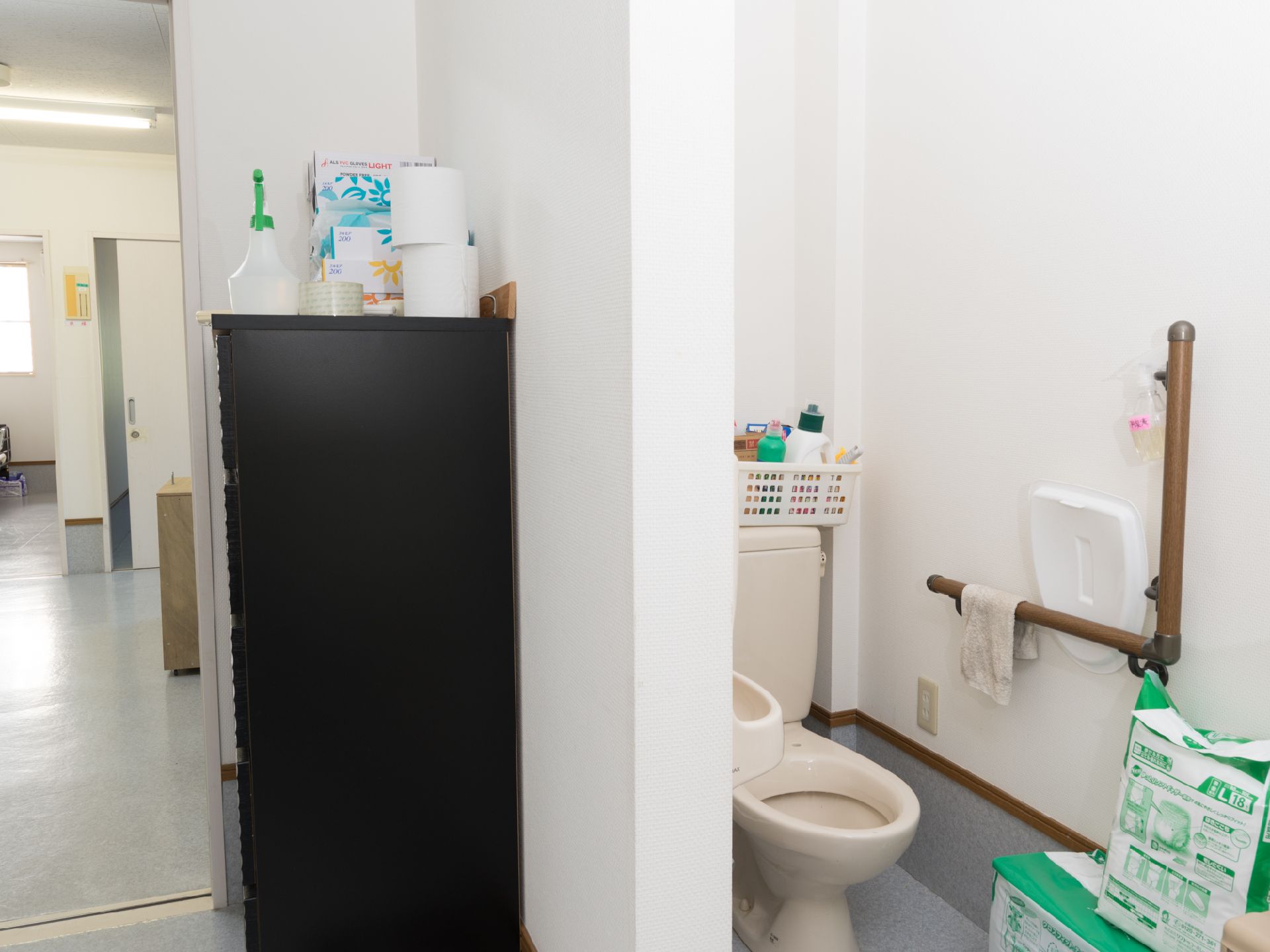 白い壁とグレーの床のトイレ。手洗いスペースがトイレ内には設けられている。壁には手すりがあり安全。
