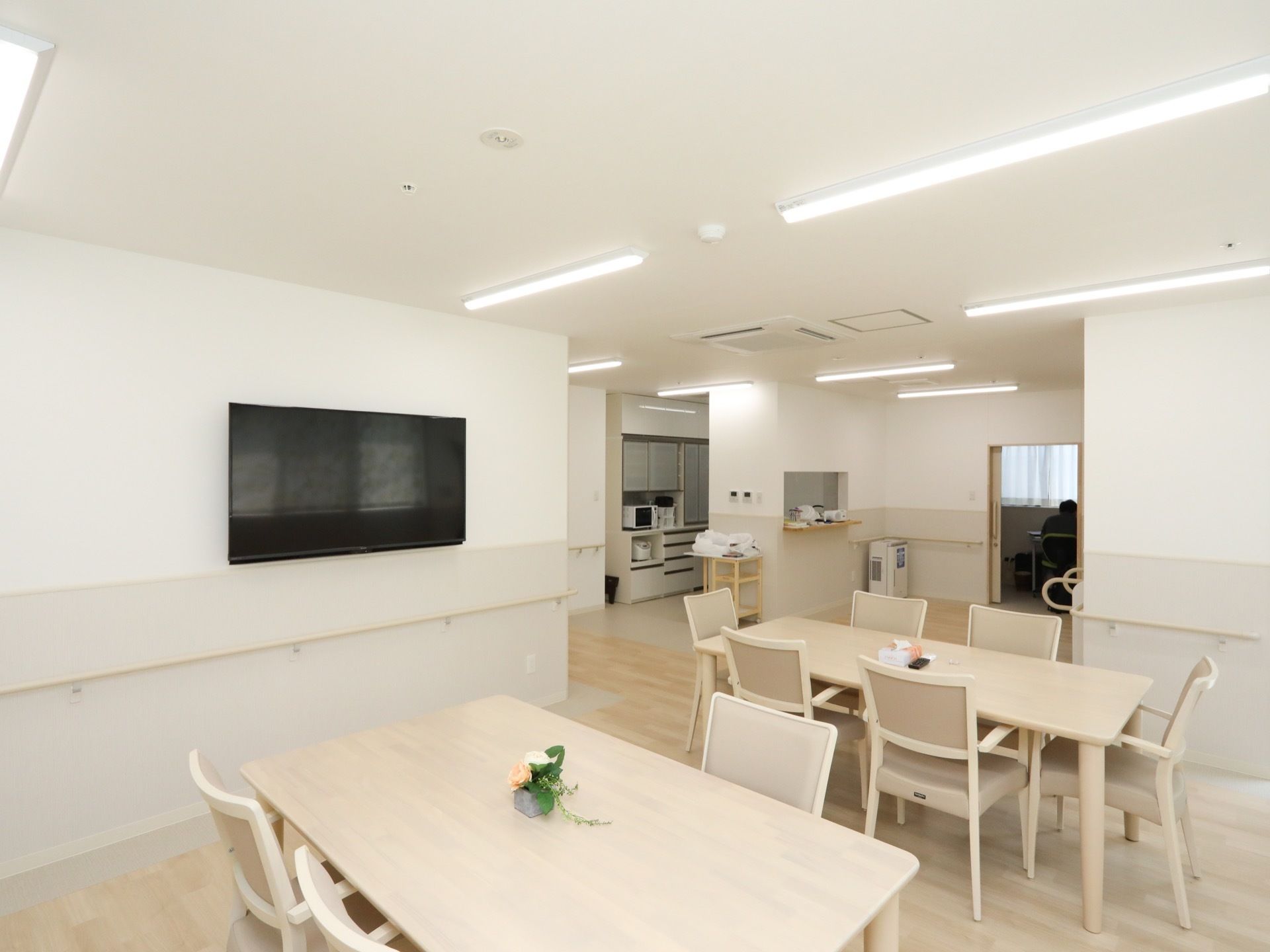 大きなテレビが設置されている食堂で、奥にキッチンが見える。食器棚には、炊飯器や電子レンジが置かれている。
