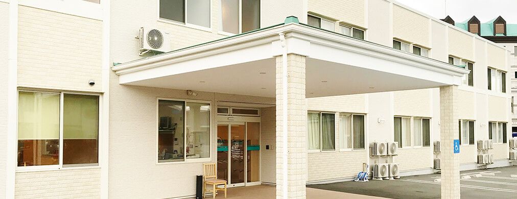 白い外壁で、入り口前に椅子が置いてある2階建て建築物