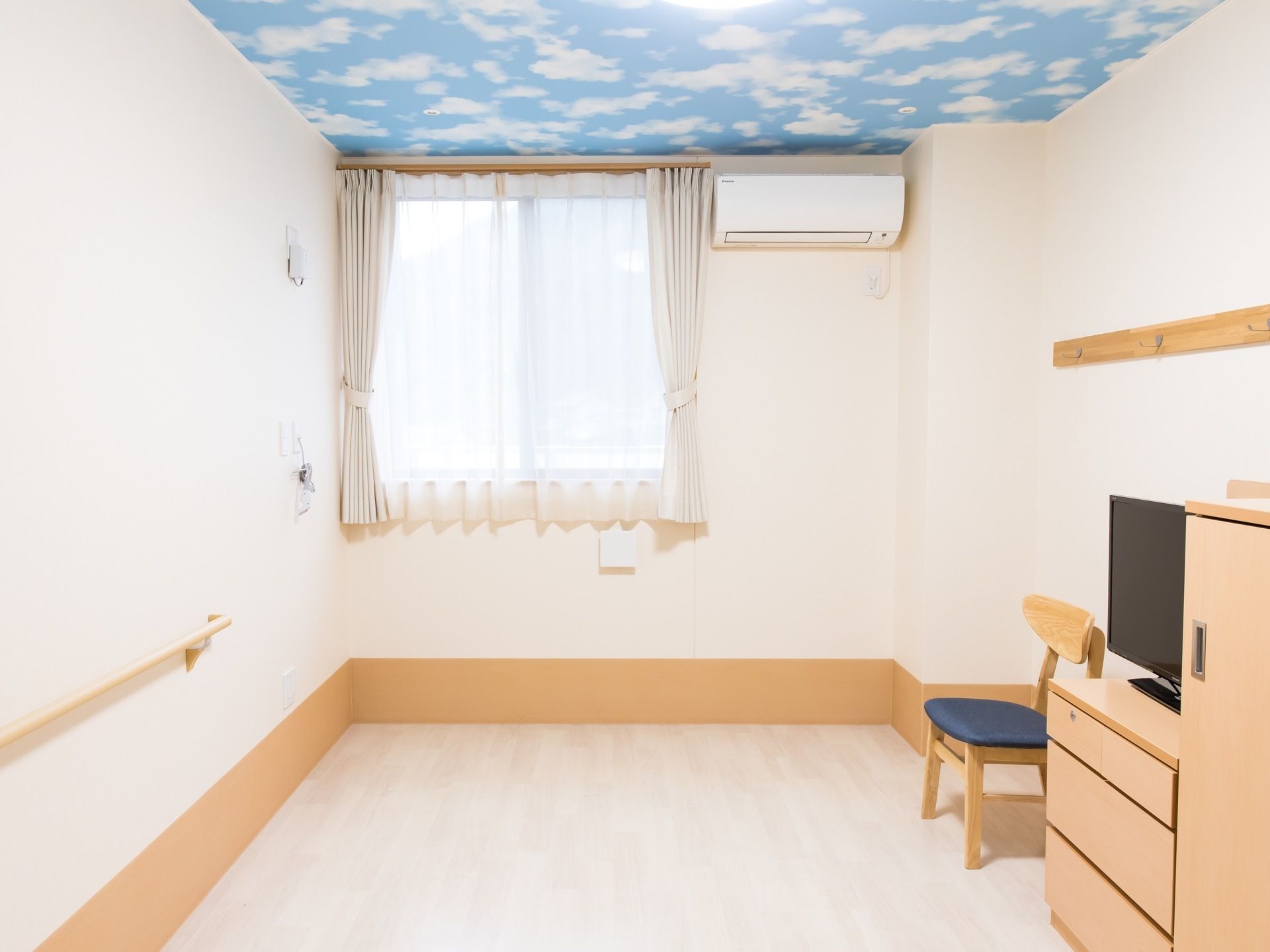 居室の天井に青空と白い雲が描かれている。白色の壁と家具の明るい色づかいのコントラストが美しい居室になっている。