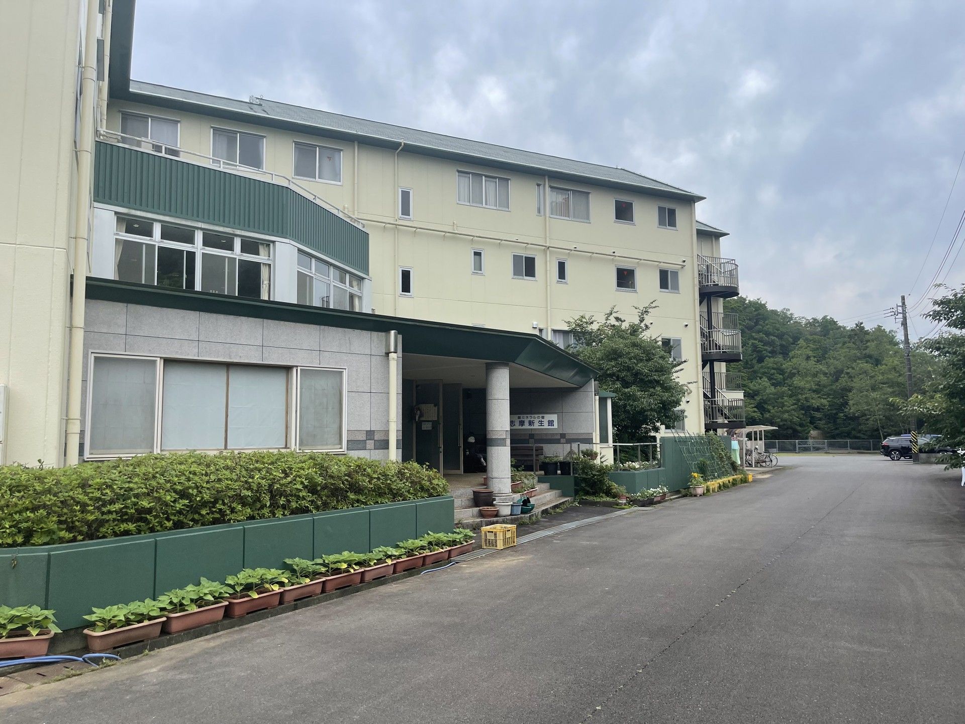 志摩新生館の看板とお出迎えの人形がある、4階建ての建物