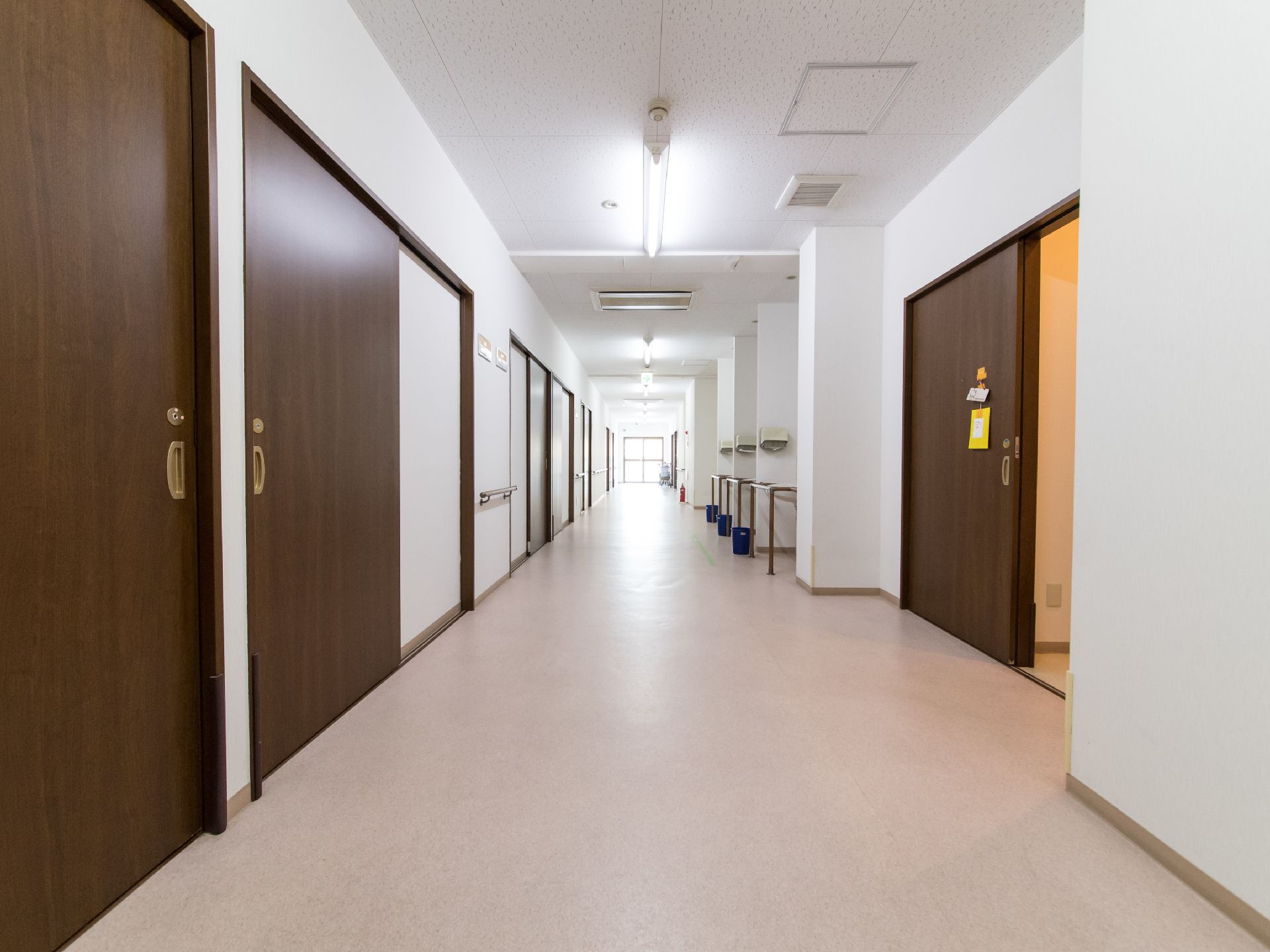白い壁にダークブラウンの幅の広い扉が映える広々とした廊下。廊下の所々に洗面スペースが設置されている。
