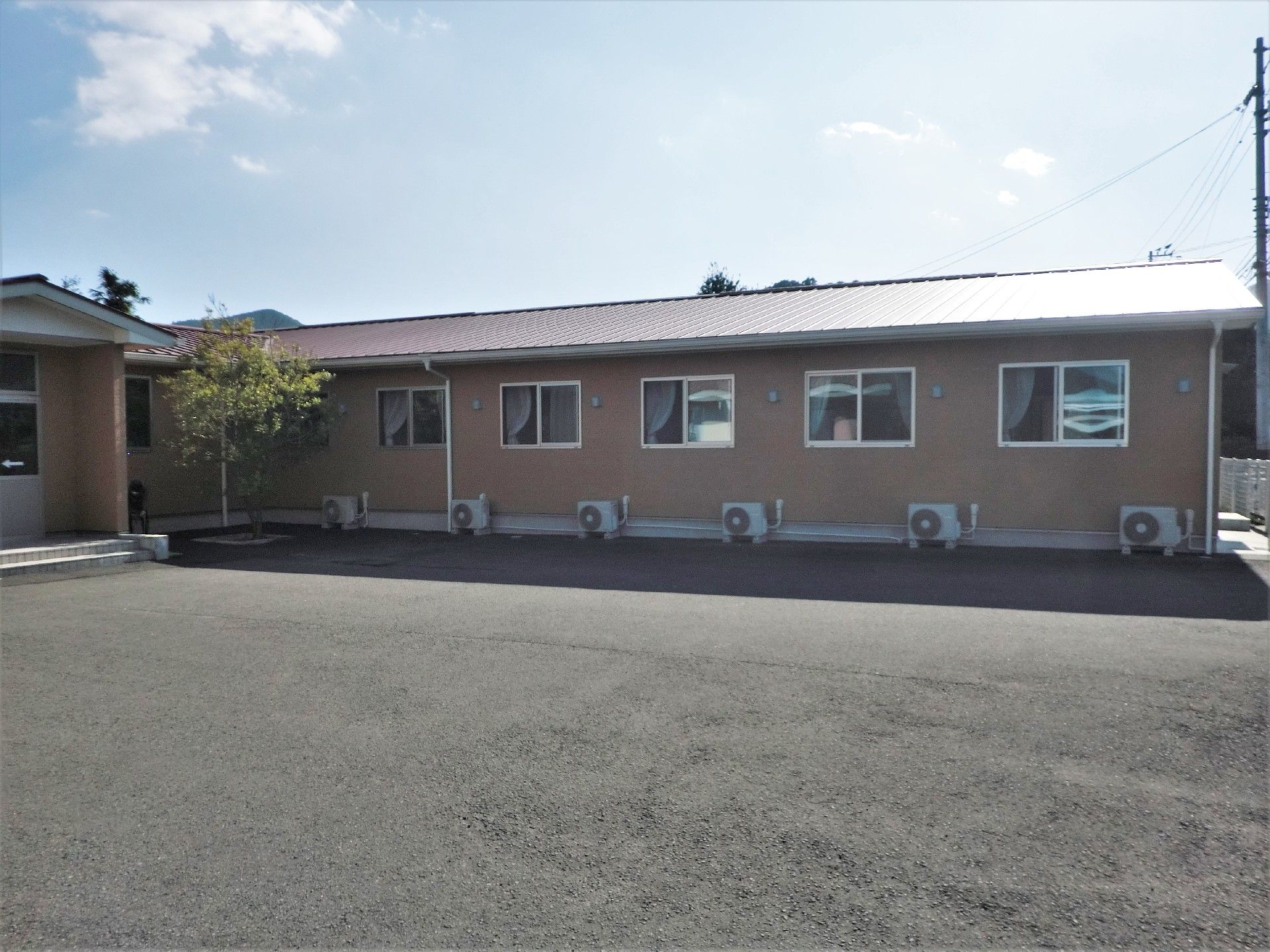 日当たりが良い場所に建つ平屋建ての建物。手前に広がる駐車場スペースから施設の全景を写した写真