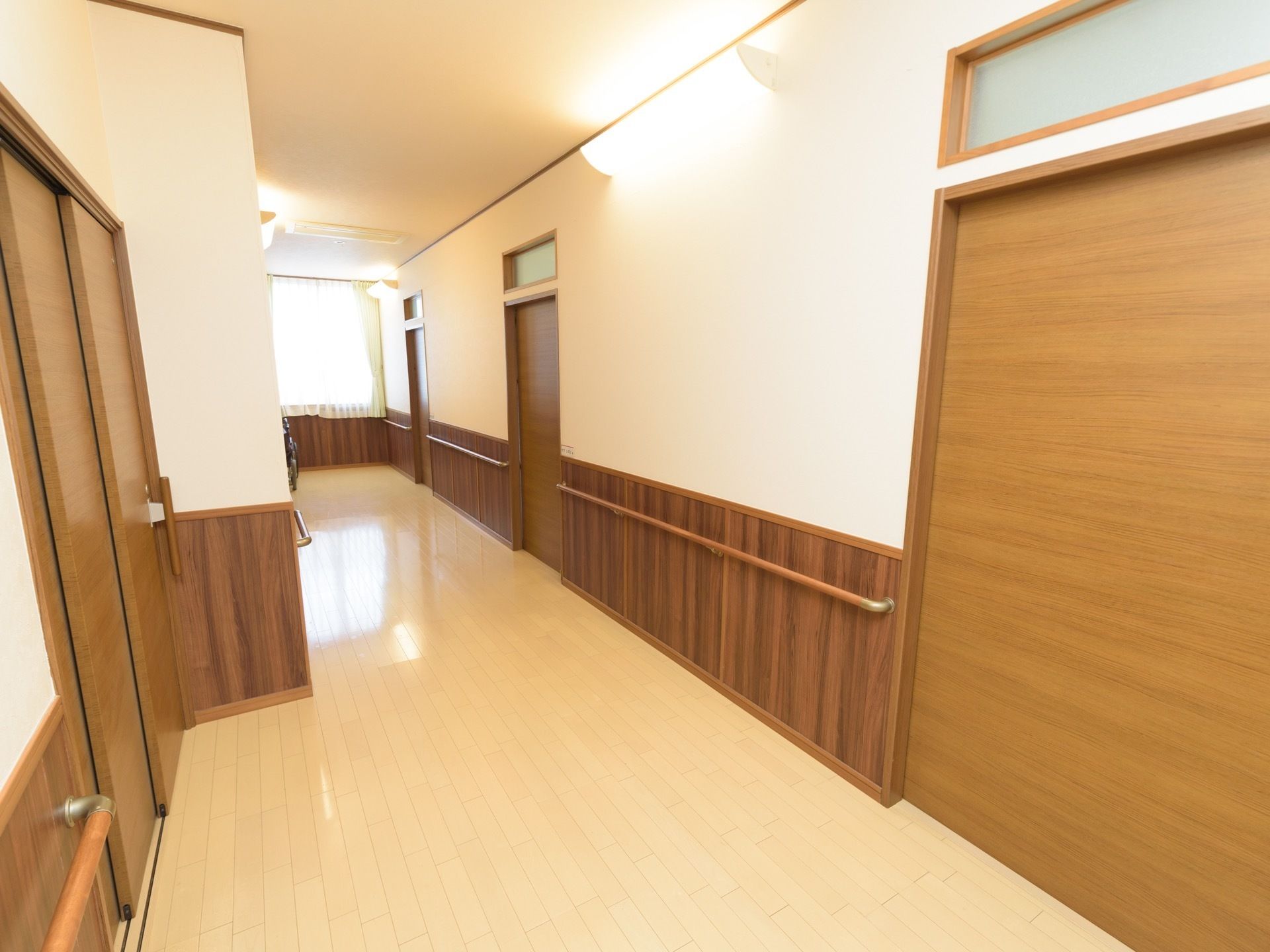 廊下は、壁の上部に設置された大きな照明や、窓からの採光で明るくなっている。居室入口以外の壁には手すりが設置されている。
