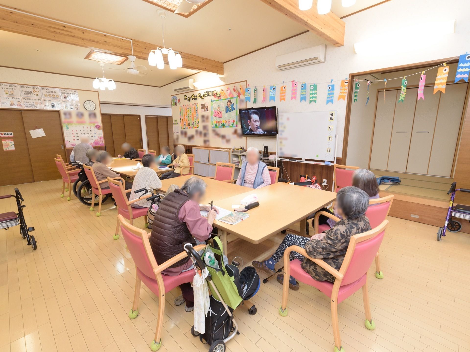 共有スペースに多くの椅子やテーブルがあり、入居者様が集まっている。テレビを見たり、何かを書いたりしている。