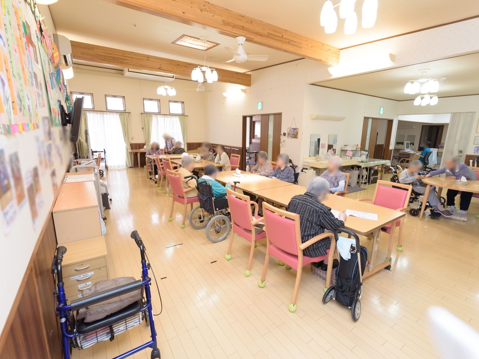 食堂に多くの椅子やテーブルが置かれていて、入居者様が集まっている。車椅子のままでテーブルについている入居者様もいる。
