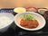 ソースがたっぷりとかかった肉料理に野菜が添えられ、汁物や白いご飯、野菜のお和え物や漬物などが並んでいる黒いトレー。