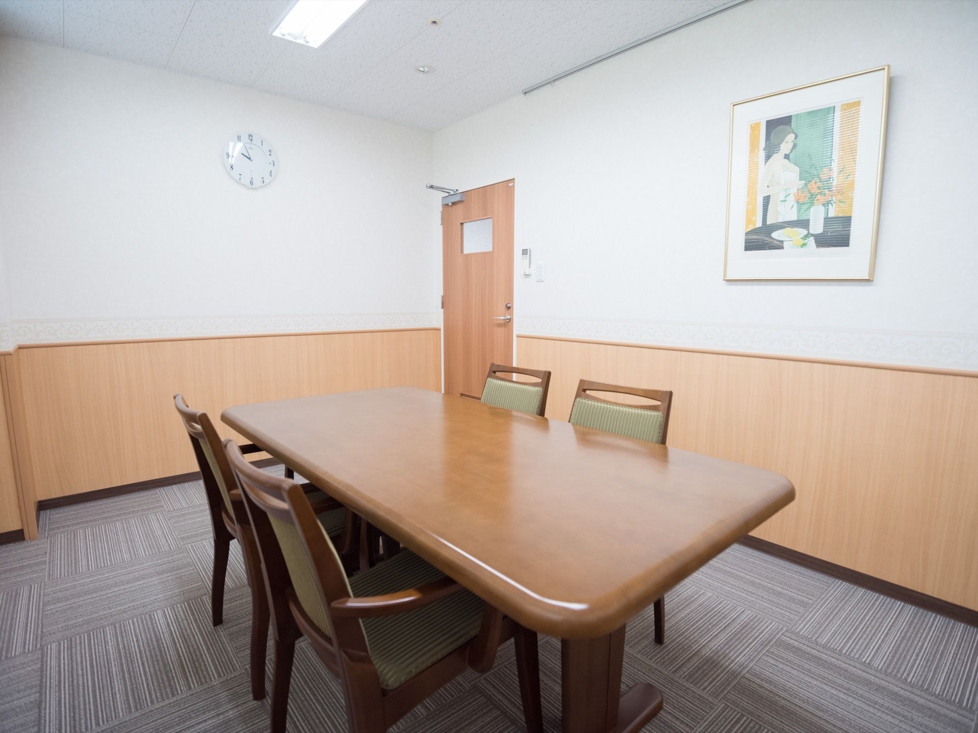 グレーのタイルカーペットが敷かれた小部屋がある。4人掛けのテーブルセットが置かれ、壁には絵画や時計が掛けられている。