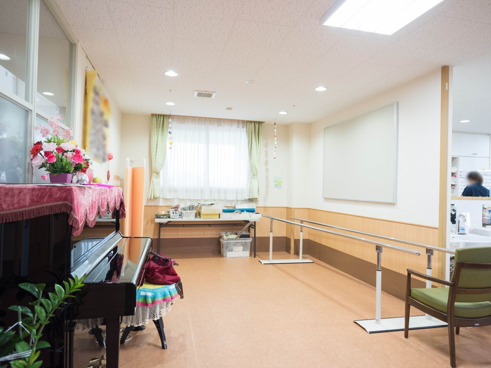 歩行訓練用の手すりが設置されたフロアがある。反対側の壁際にはピアノがあり、掲示板には写真がたくさん飾られている。