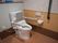 便座に手すりと背もたれの付いたトイレがある。壁には手すりや操作パネルの他、ナースコールがある。
