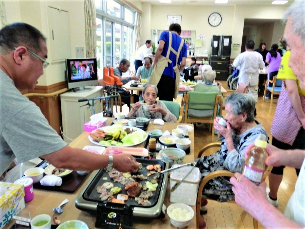 テーブルの上には焼き肉をする大きなホットプレートが置かれ、食事を楽しんでいる入居者たち。