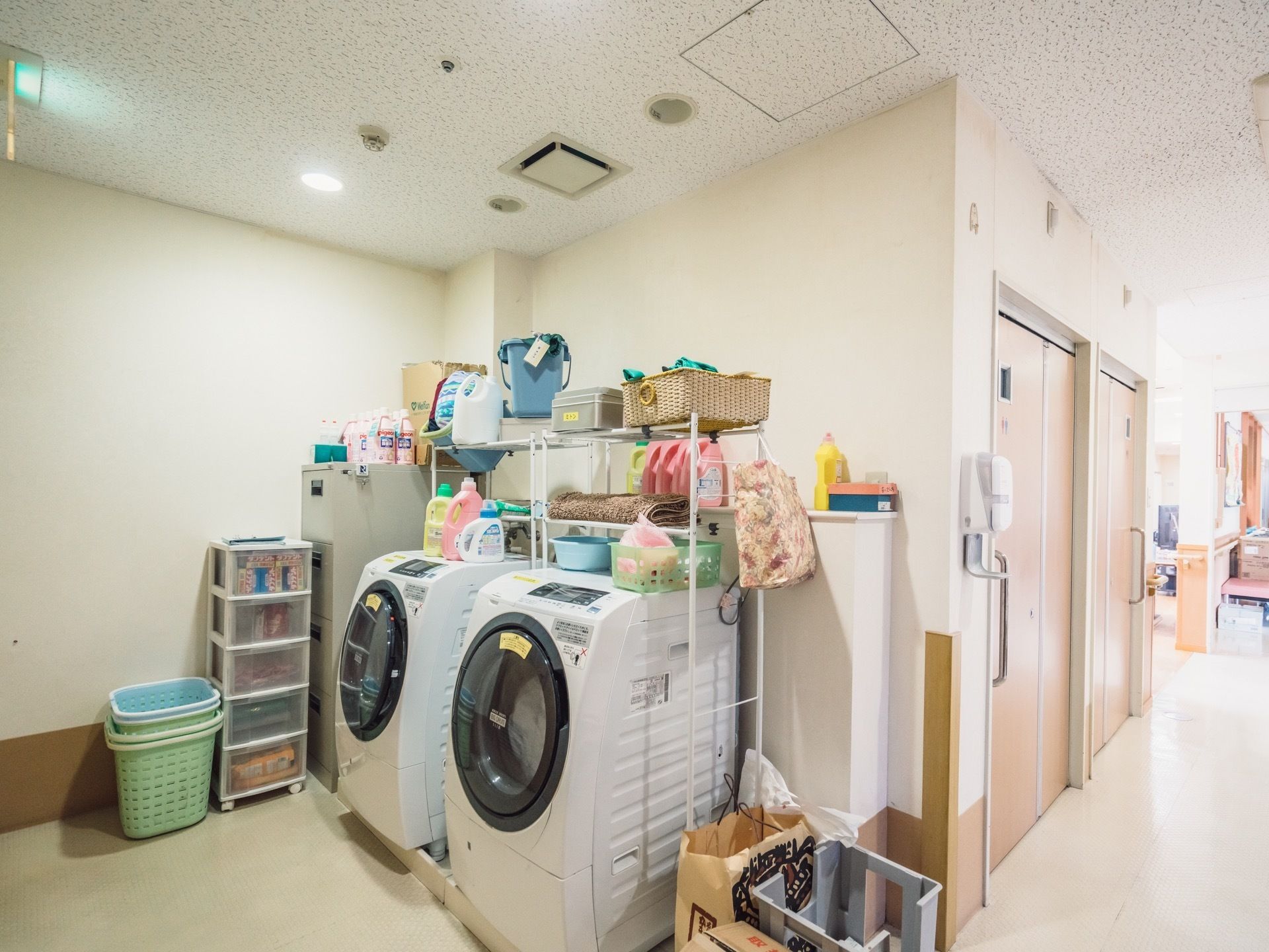 室内の一角に大きなドラム式洗濯機を2台配置されている。機械の上に取り付けられた棚には、すぐ使用できるように洗剤などの備品が収納してある。