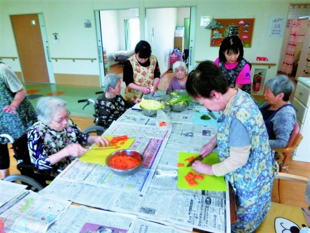 新聞紙の上にプラスチック製のまな板を置き、熱心に野菜を刻んでいる女性入居者たち。