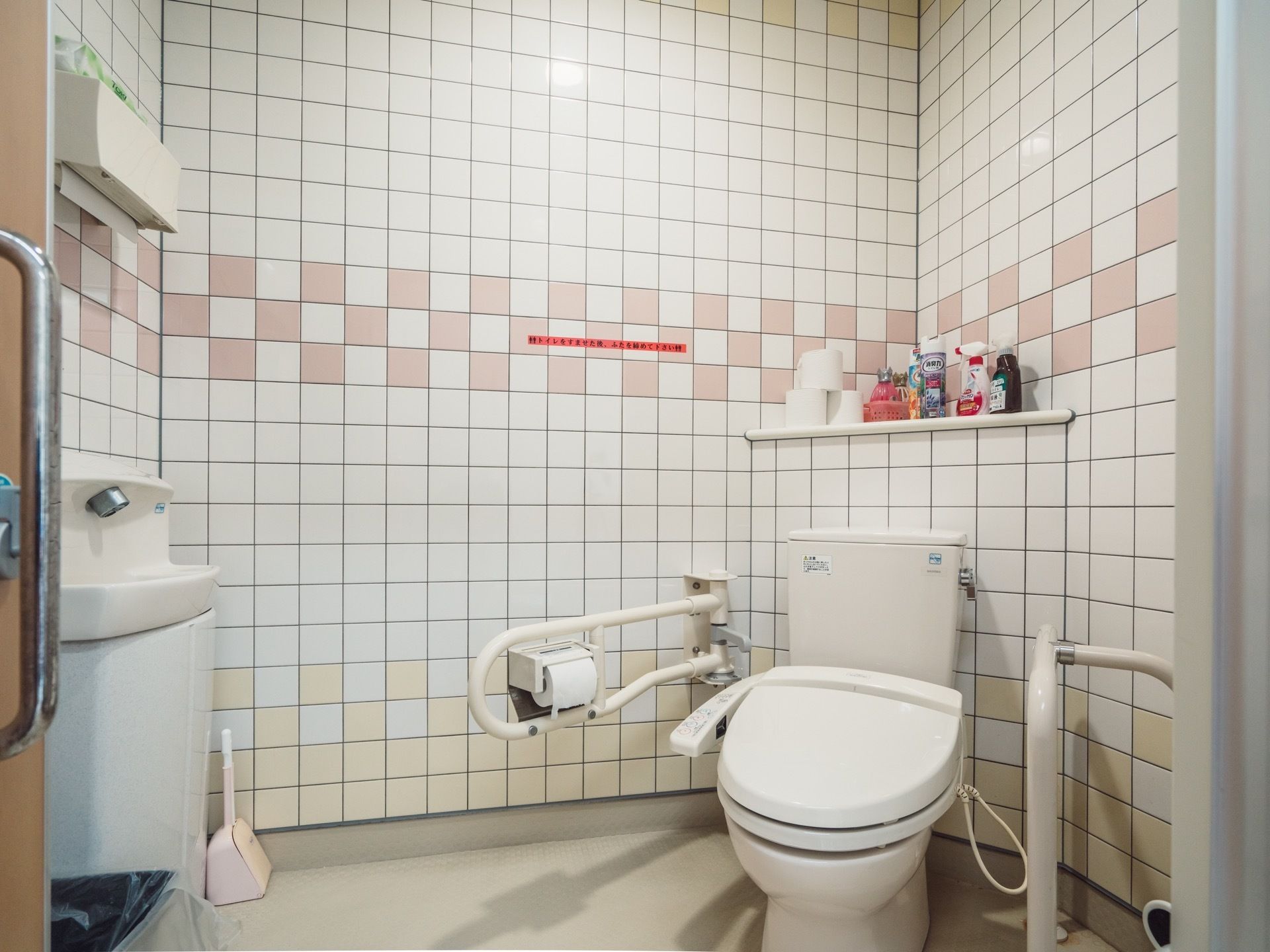 タイル張りのトイレスペースの角に、洋式便器が設置されている。便器の左右に白い手すりが取り付けてある。