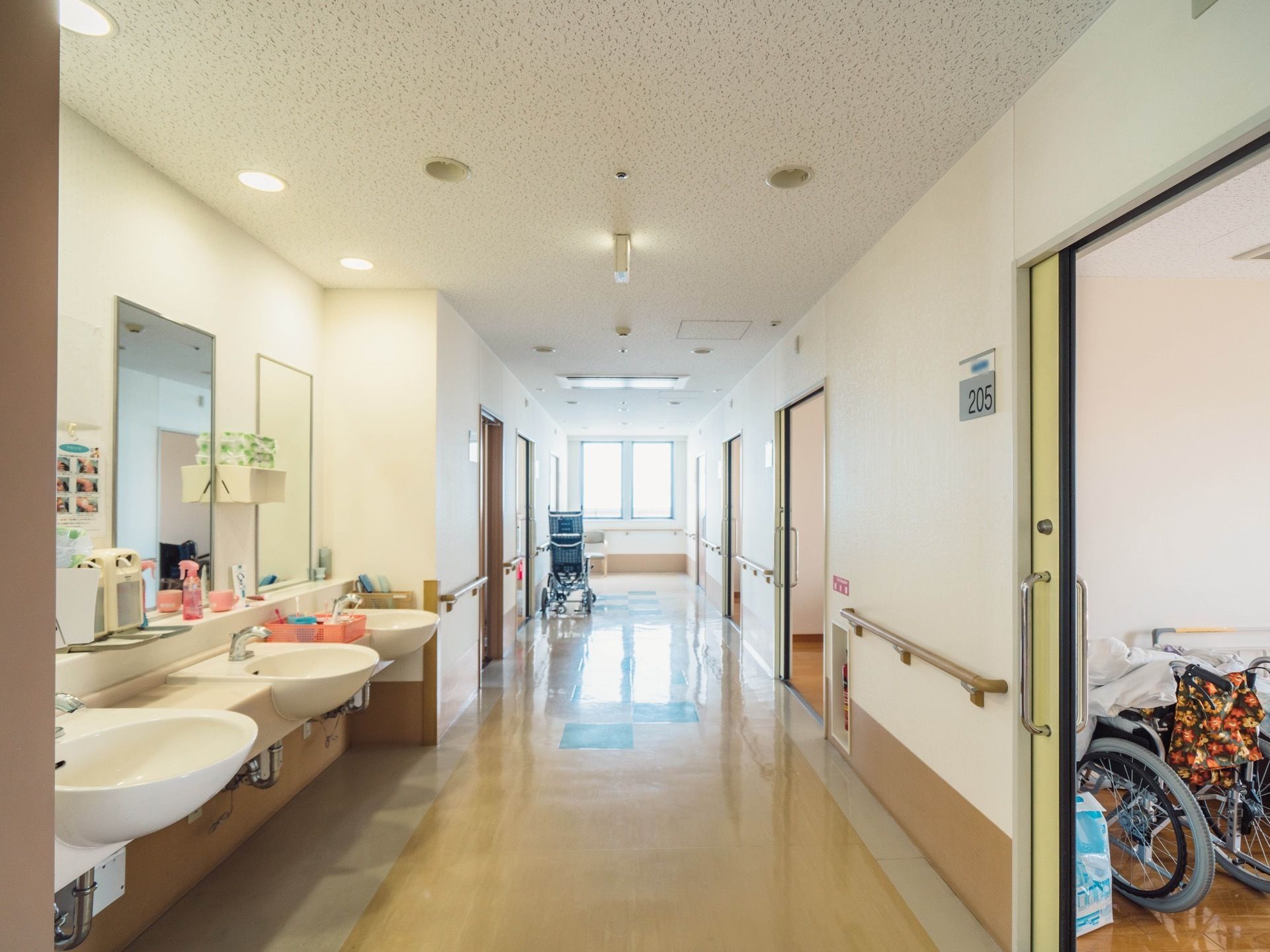 居室の扉が並んでいる廊下の一角が広くなっており、丸みを帯びた形状の洗面台と四角い鏡が３セット設置されている。